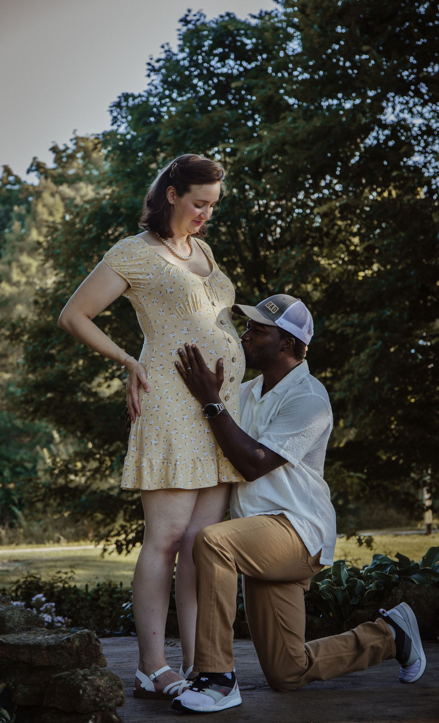A tender maternity moment captured outdoors as an expectant couple shares a gentle embrace in natural lighting.