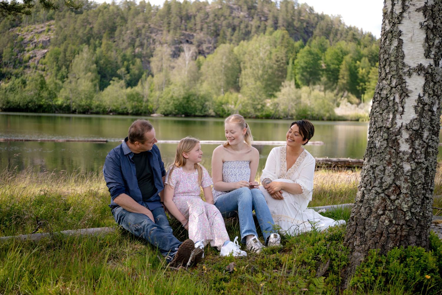 Family sitting together on grass near a lake during a sunny summer afternoon.