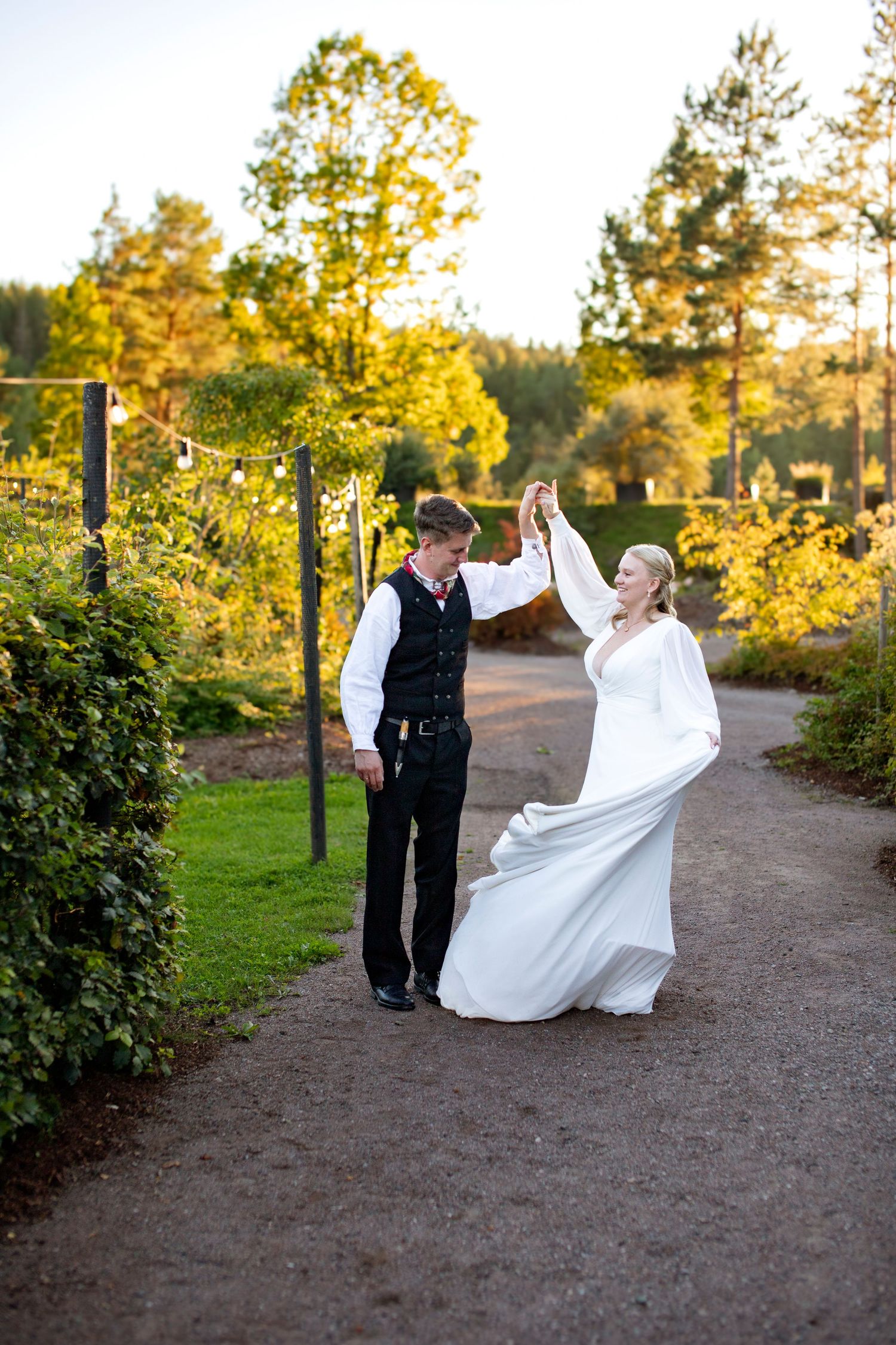 A couple dancing together on a garden path during golden hour sunset with autumn trees in the background.