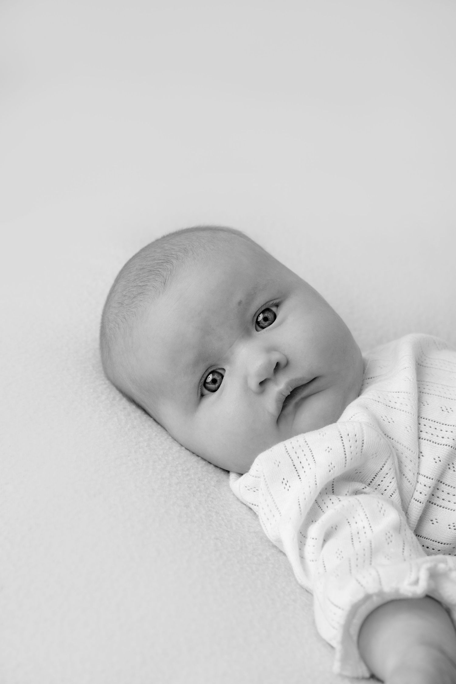 A black and white portrait of an infant wearing a white knit sweater while lying down.