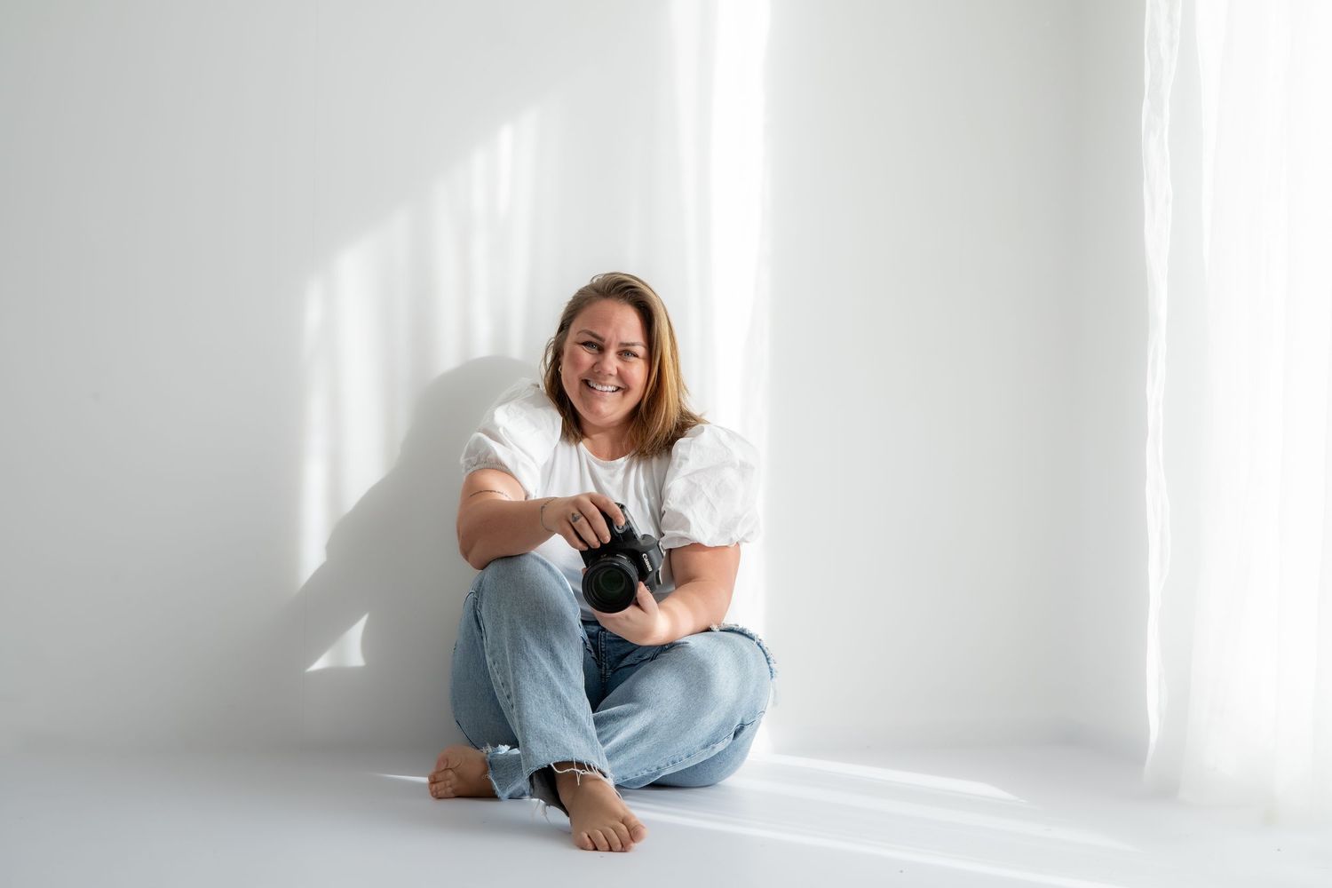 Person in casual attire sits in bright white room with sunlight streaming through windows, creating minimalist aesthetic.