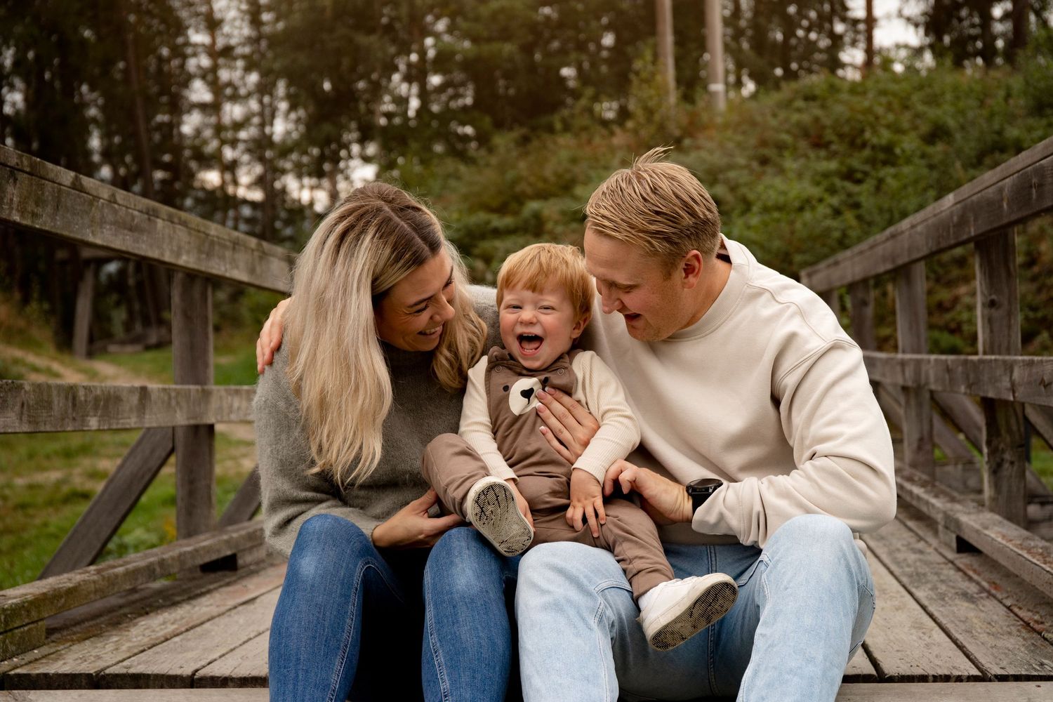 A happy family shares joyful moments together while sitting on a rustic wooden bridge in a forest setting.