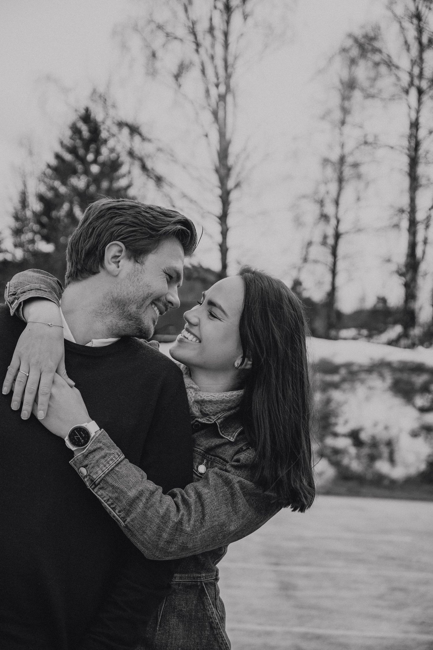 Romantic winter couple embracing outdoors with snow-covered trees in background.