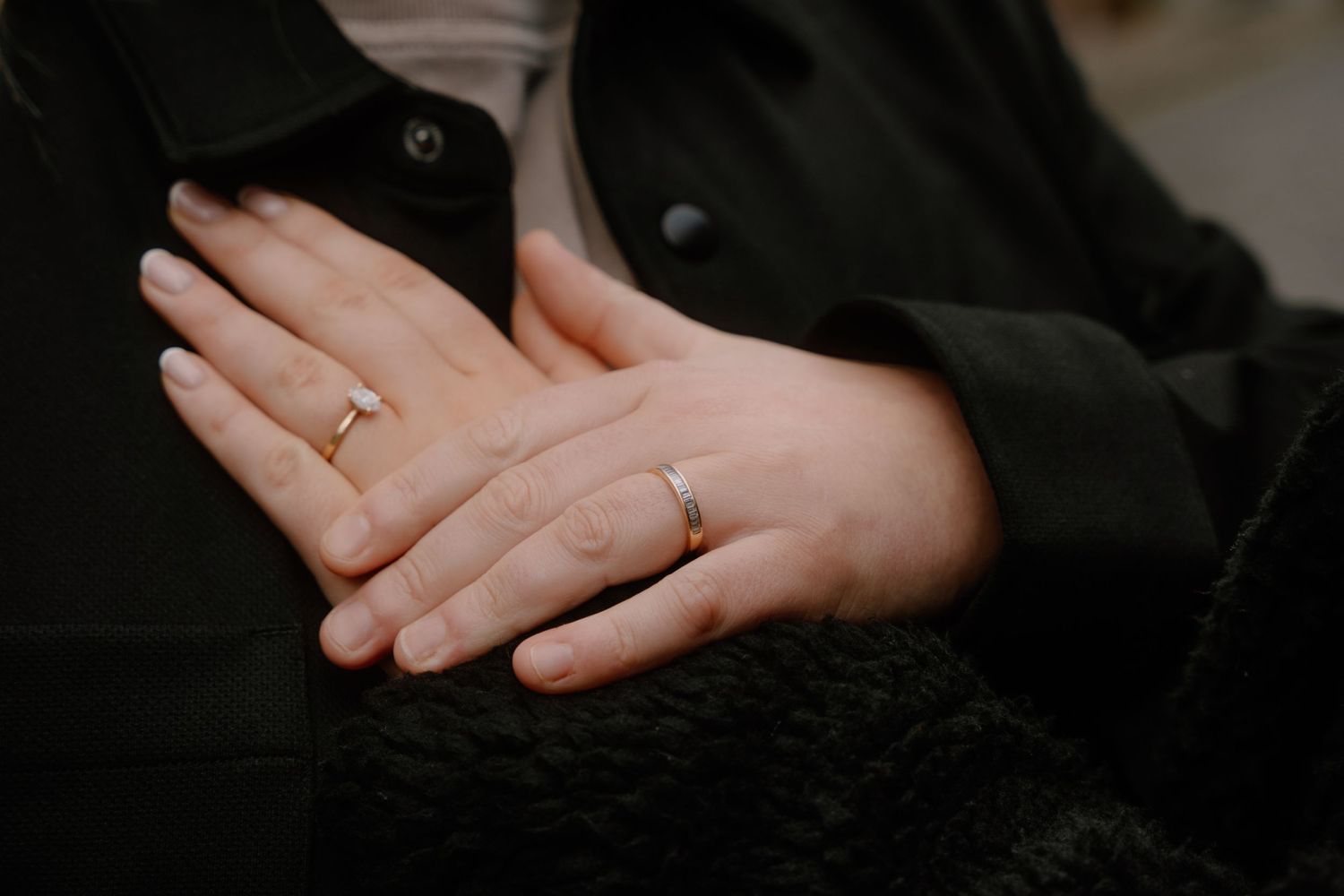 Close-up of hands displaying engagement or wedding rings against black clothing.