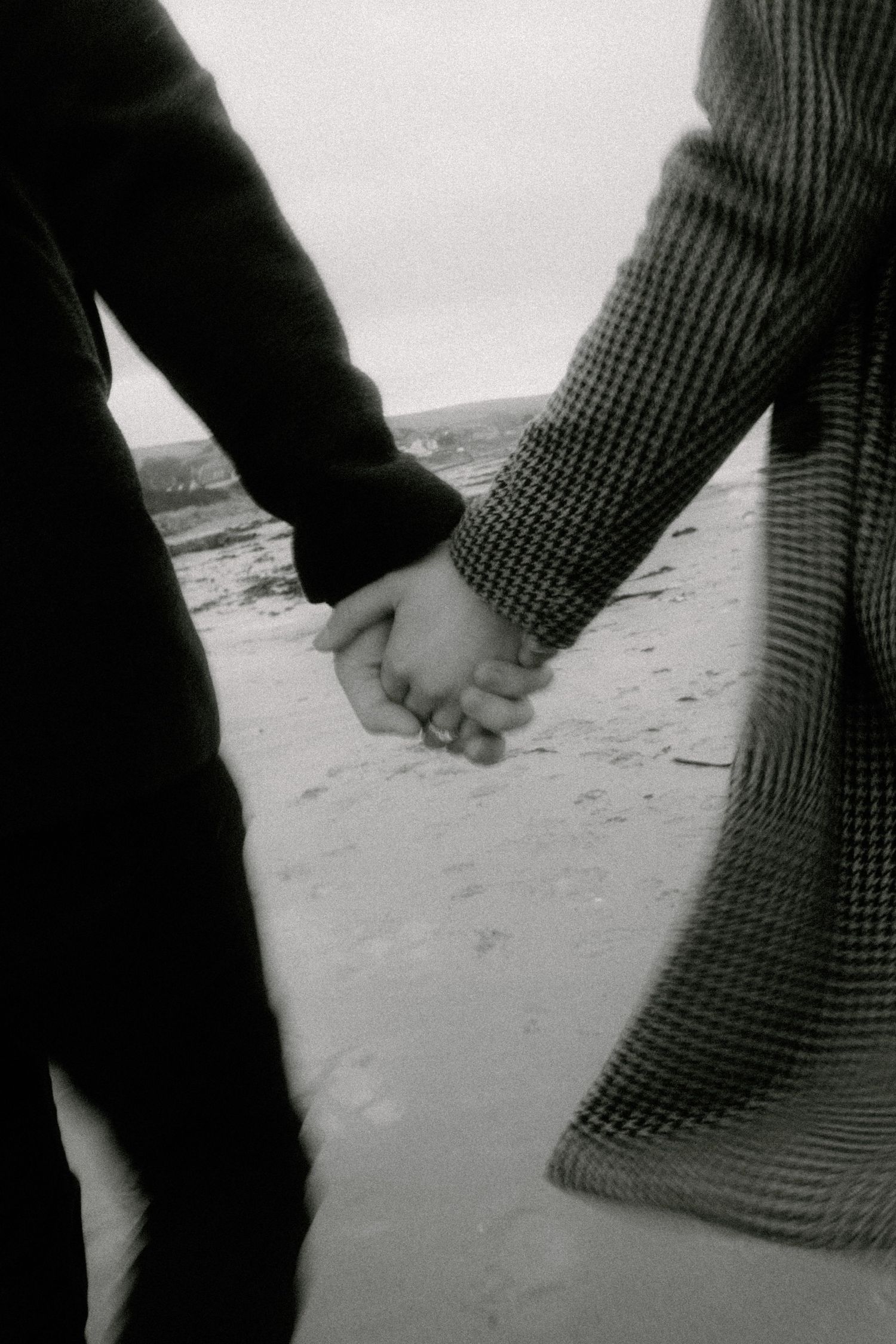 A romantic black and white image of two people holding hands on a beach.