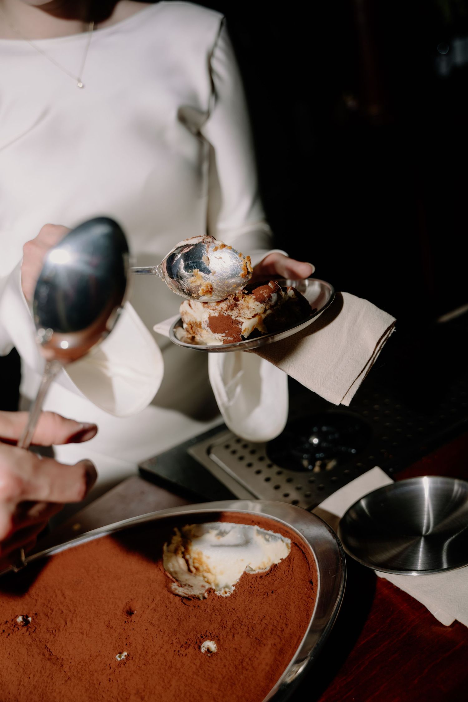 Server presenting a plated tiramisu dessert dusted with cocoa powder at an elegant restaurant.