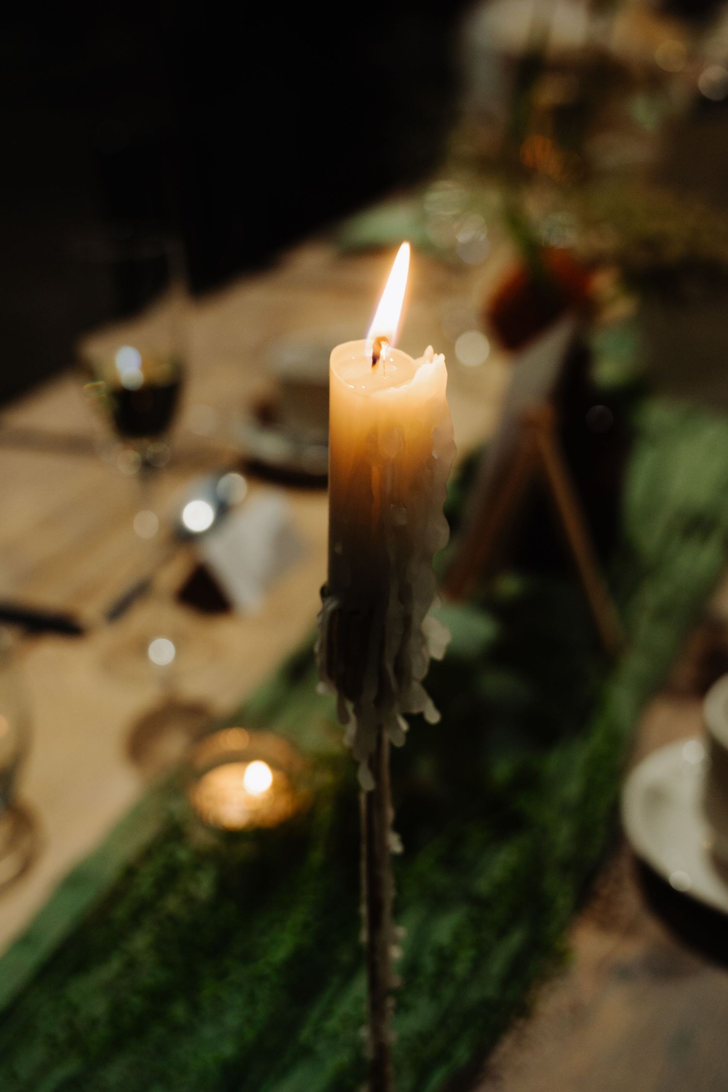 A row of lit white candles with melted wax dripping down their sides creates an atmospheric glow against greenery. Glasgow Engine Works