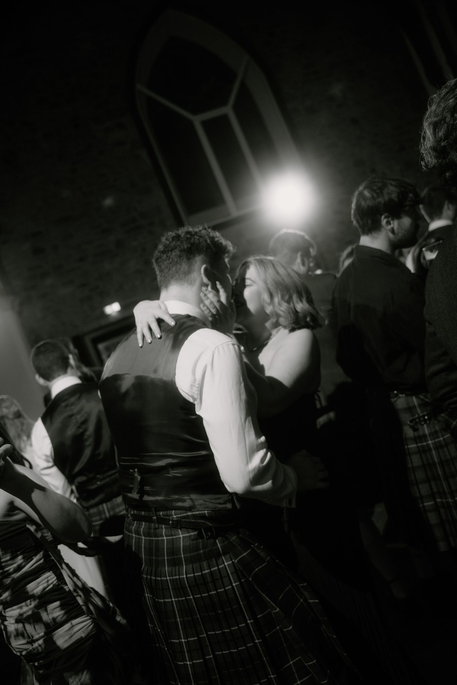Couples slow dancing in formal wear and kilts under dramatic lighting at an indoor venue.