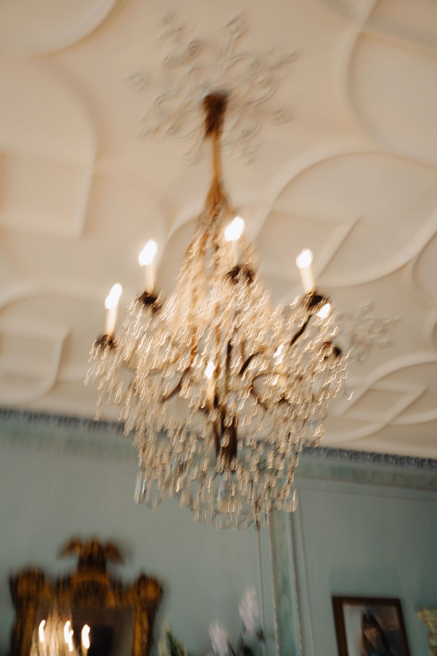 Crystal chandelier hanging from ornate white ceiling with decorative molding and soft turquoise walls in elegant room.