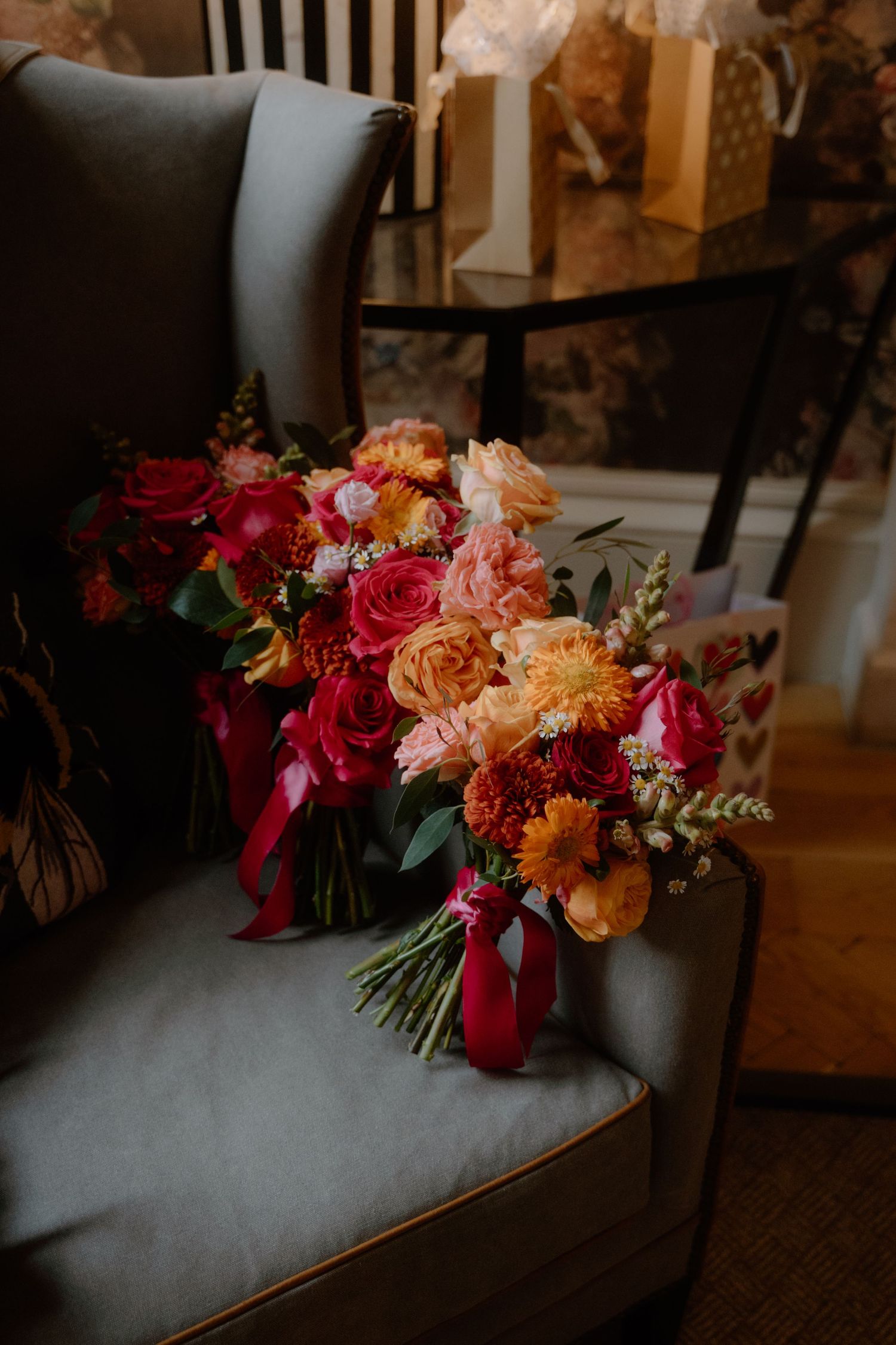 Vibrant autumn-colored wedding bouquet with roses and dahlias resting on gray chair.