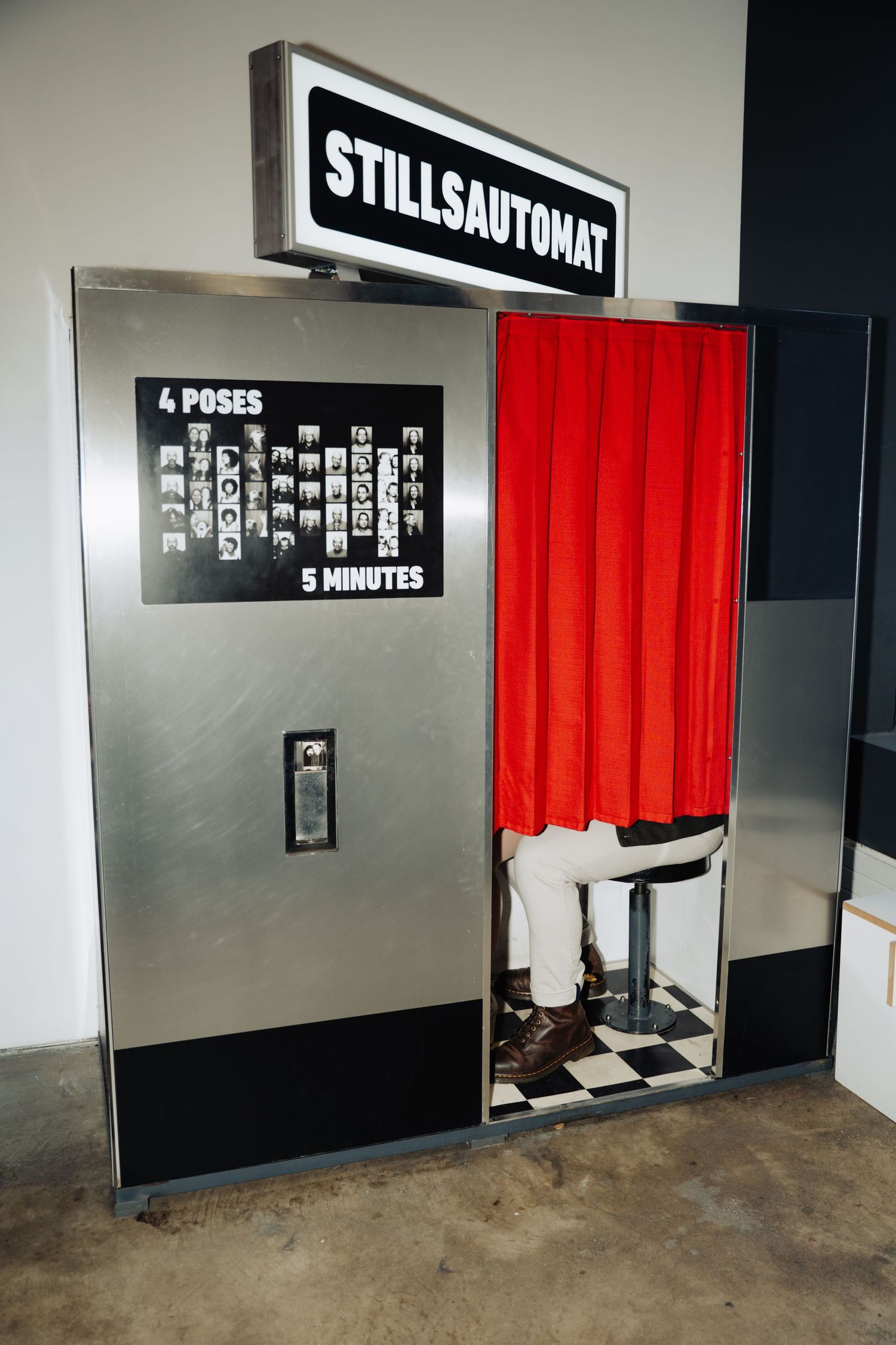 Black wall with red curtain and signage displays in a photo booth setup showing different poses and photo styles.