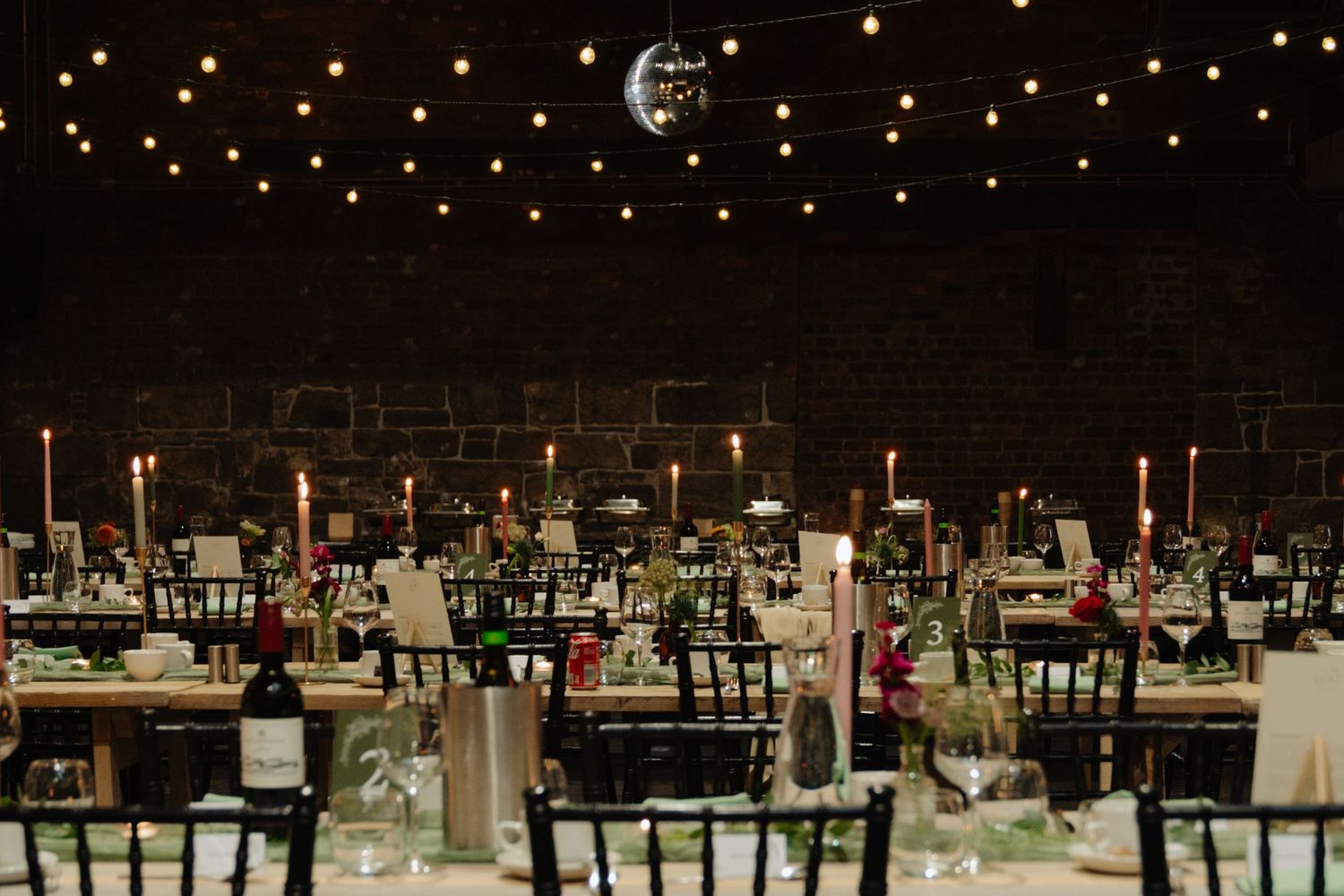 Elegant wedding reception venue with twinkling lights, round tables, and chairs arranged under a dark ceiling.