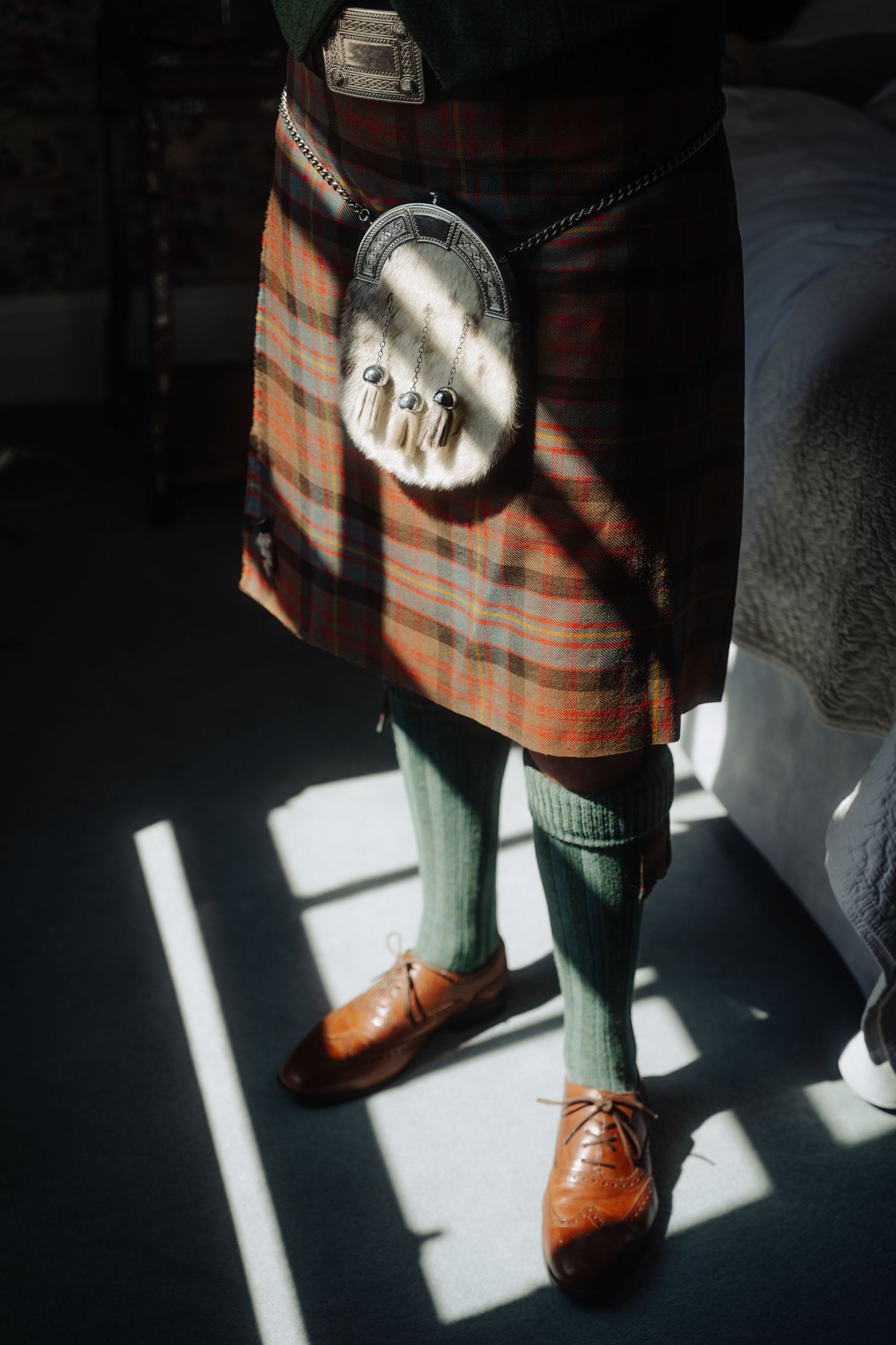 Sunlight casting dramatic shadows on a person's legs wearing plaid pants and brown leather oxford shoes.