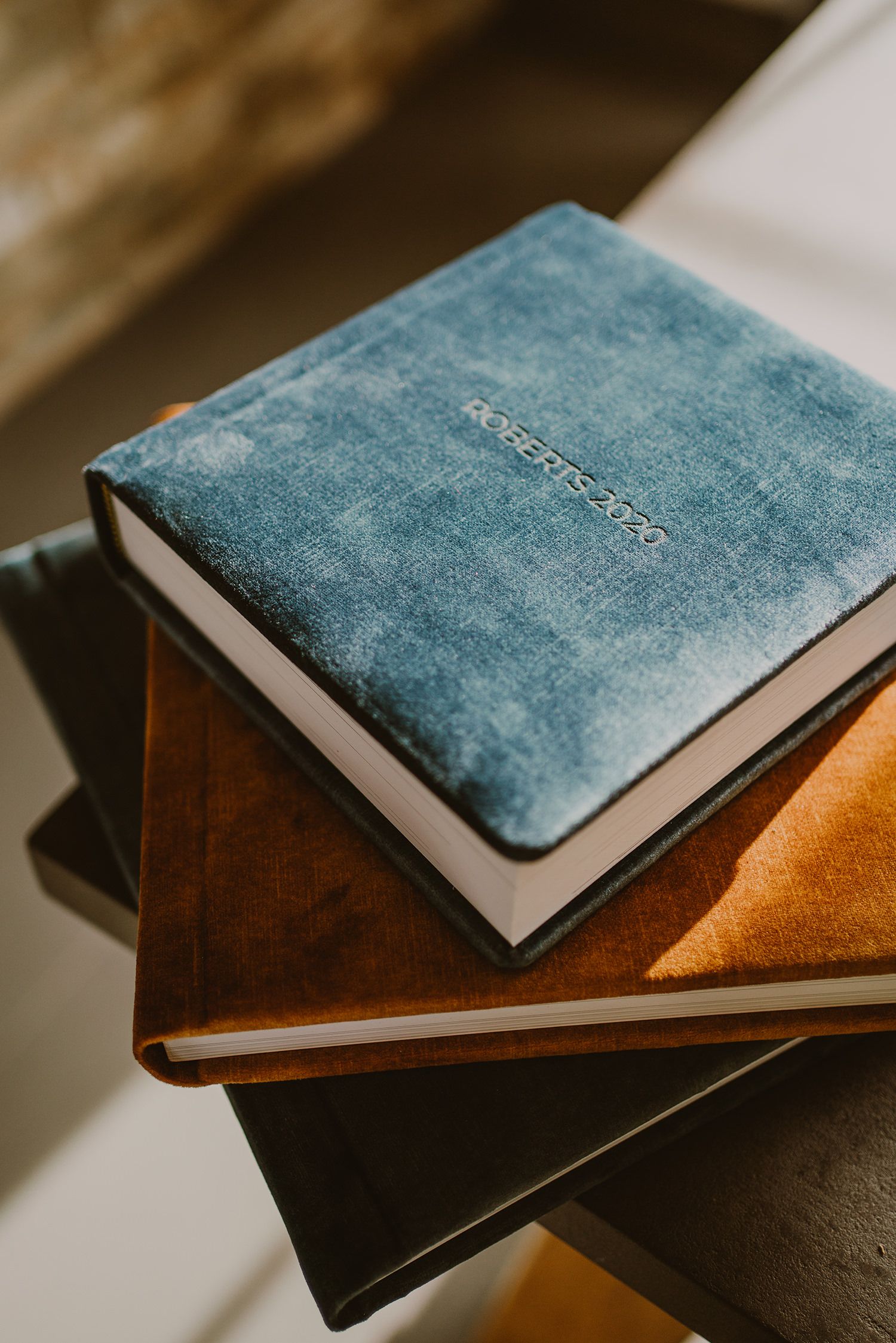 Blue velvet photo album stacked on leather-bound books.