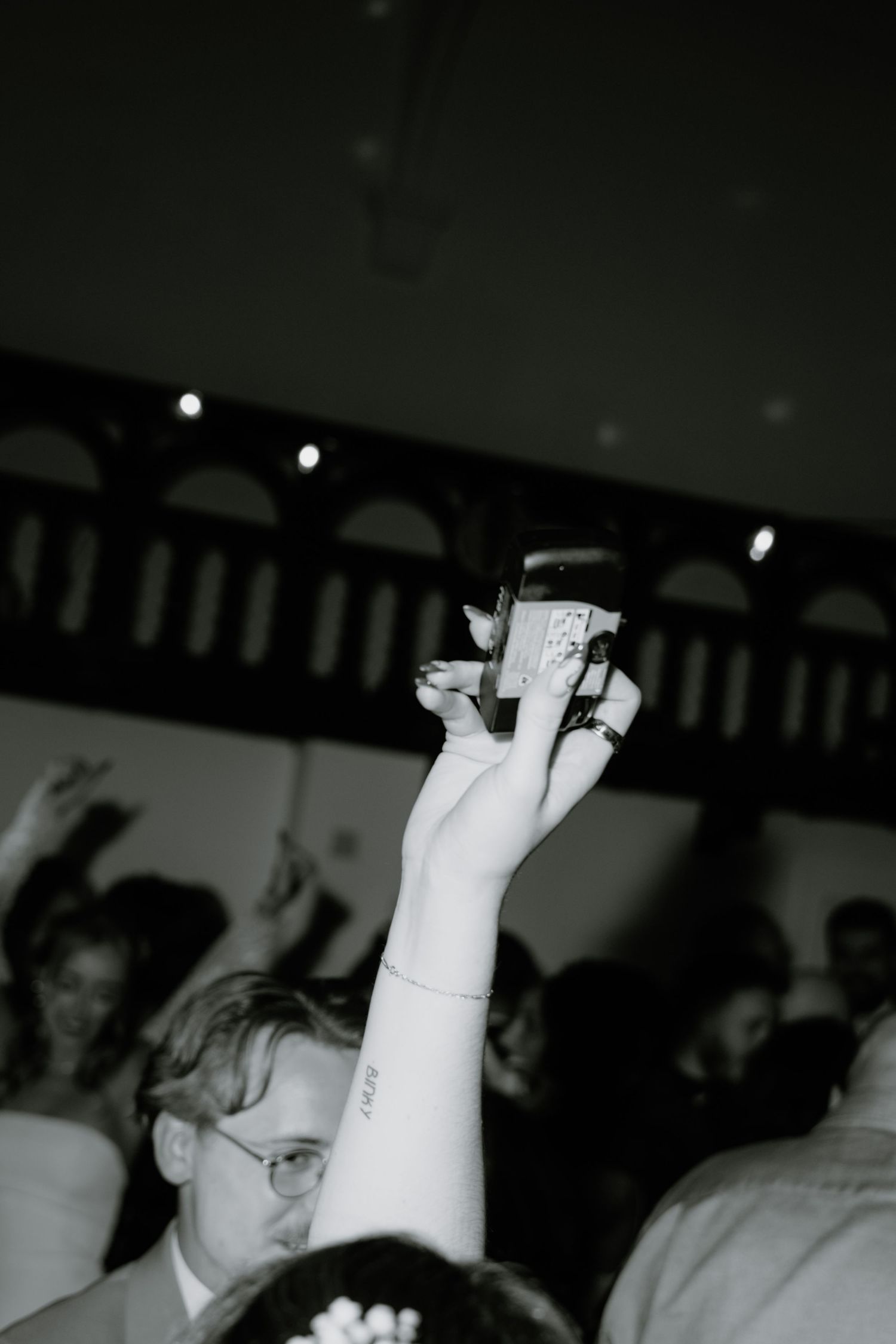 A hand raised high in the air holds a small object at what appears to be an indoor event or gathering.