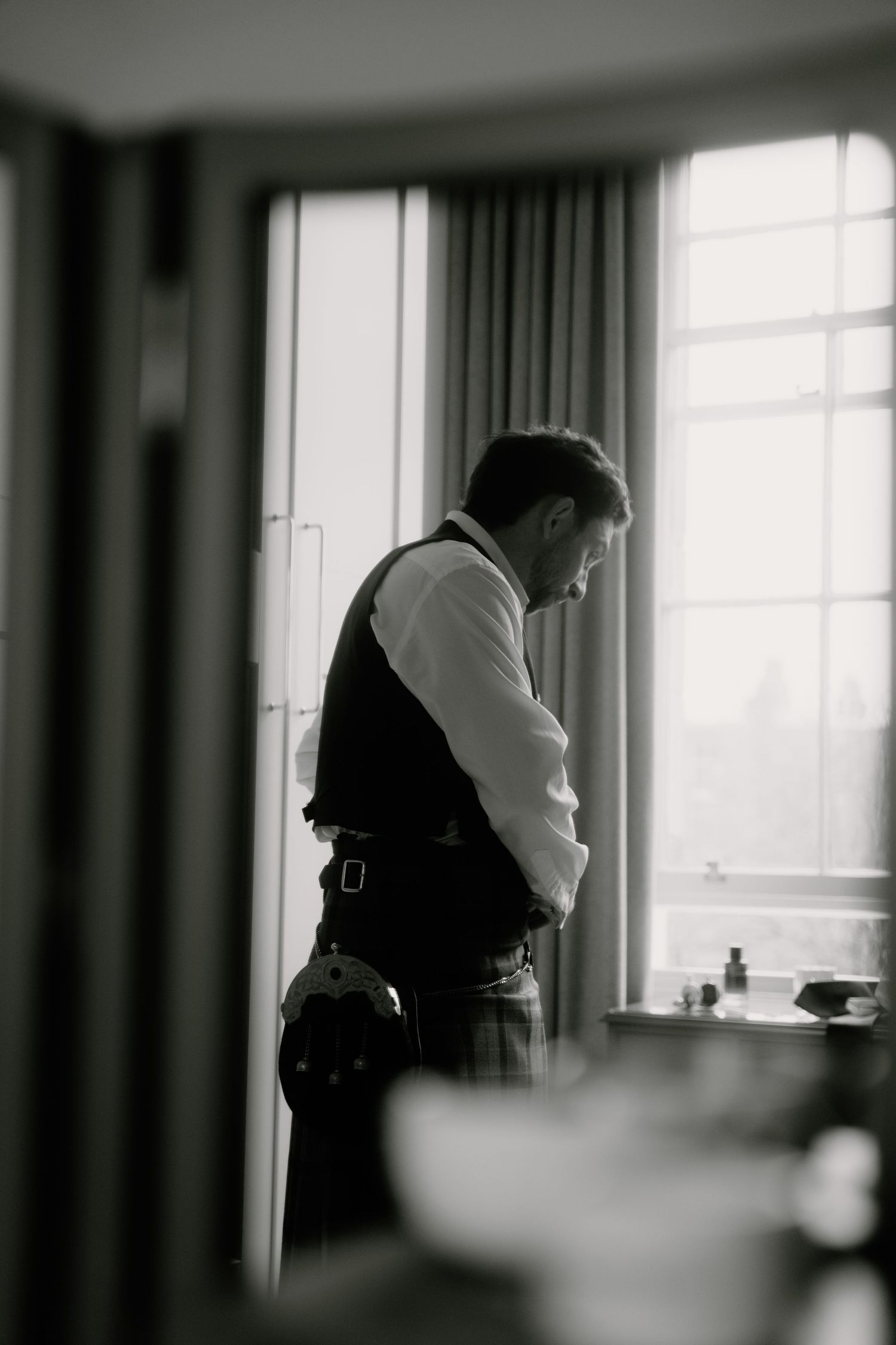 Silhouette view of someone in formal attire standing by a bright window.