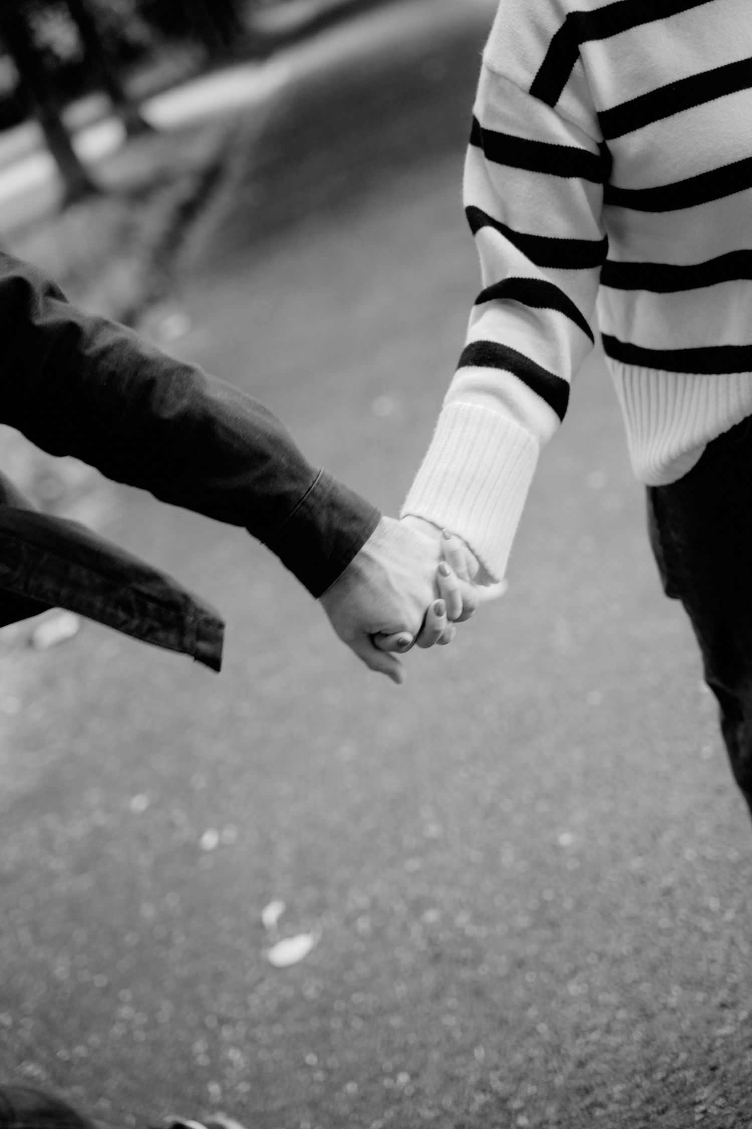 Black and white photo of a couple holding hands while walking outdoors, one wearing a striped sweater.