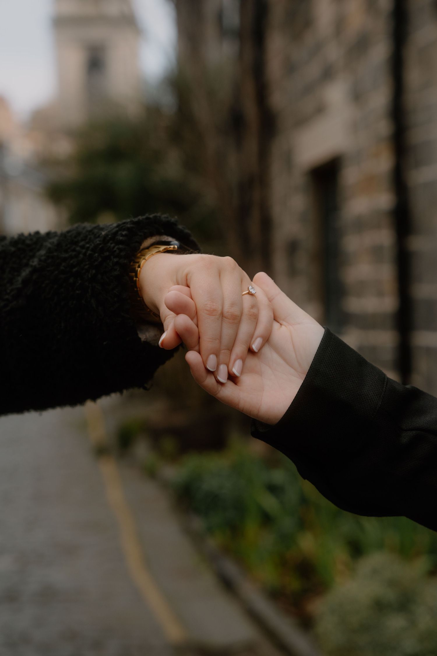 Close-up of two hands holding each other tenderly against a blurred urban background.