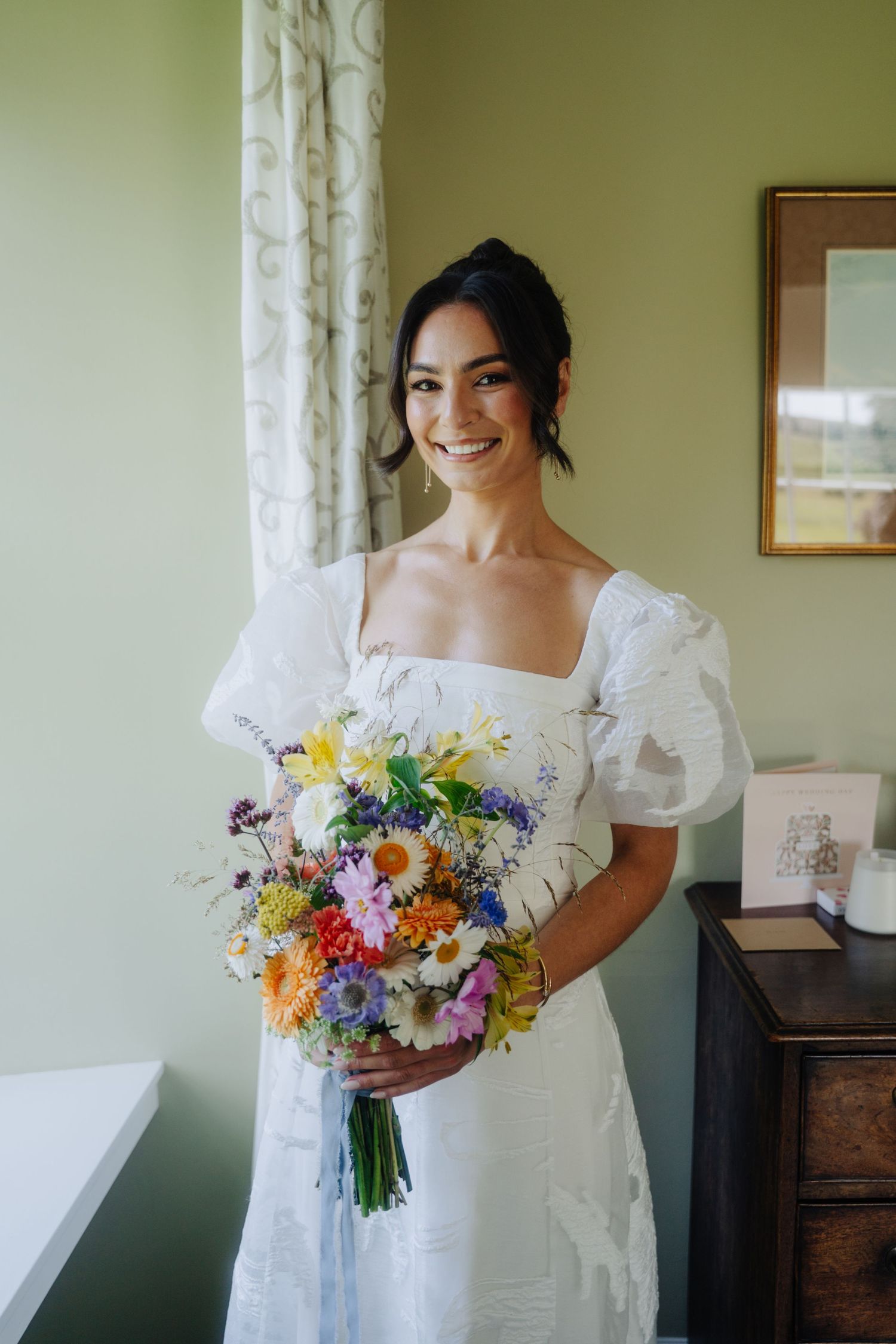 Dundas Castle A bride in a white dress holds a vibrant wildflower bouquet with colorful blooms and trailing ribbons.