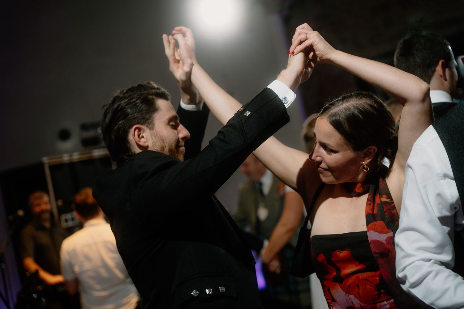 Couples dancing energetically at a wedding reception under atmospheric lighting.