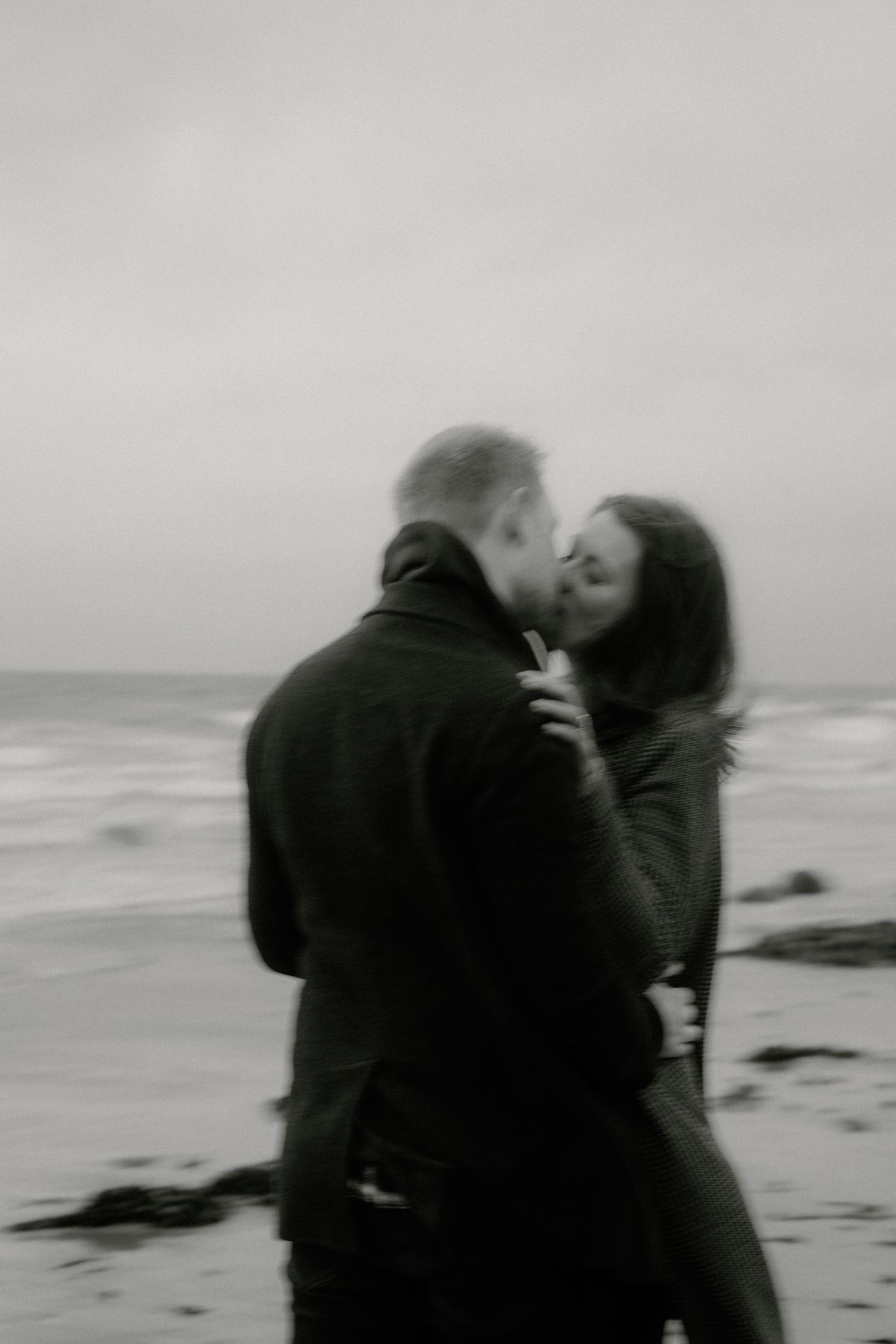 A couple in dark winter coats sharing a tender moment by the ocean.
