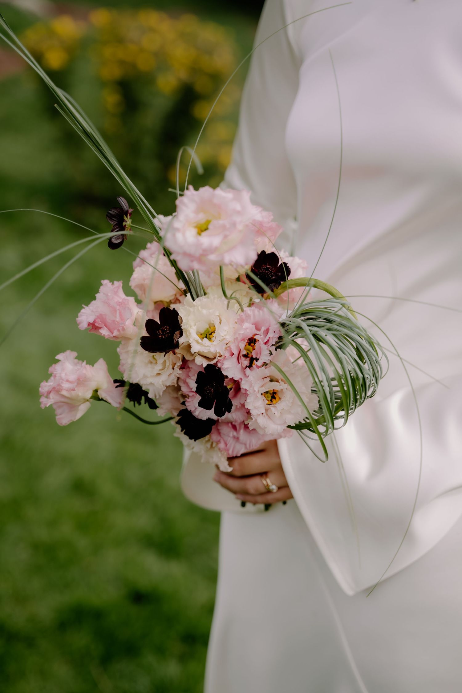 Bride in white dress holding elegant bouquet of pink, white, and dark burgundy flowers with green accents.