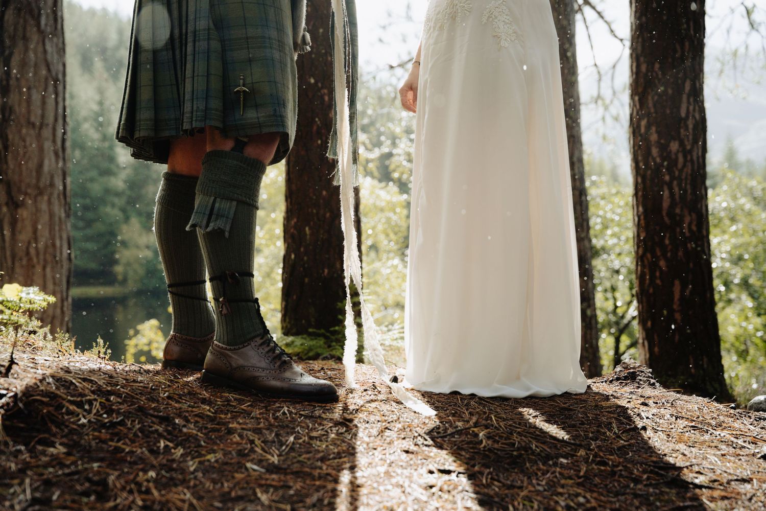 Couple holding hands in a wooded forest setting with sunlight filtering through the trees in romantic scene.