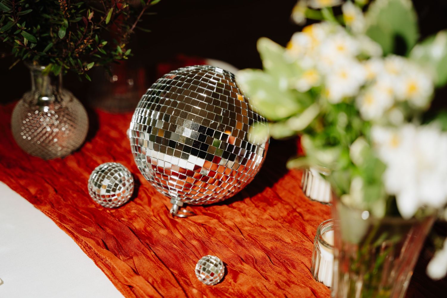 Disco balls reflect light onto a wooden surface next to white floral arrangements at a party. Glasgow Engine Works