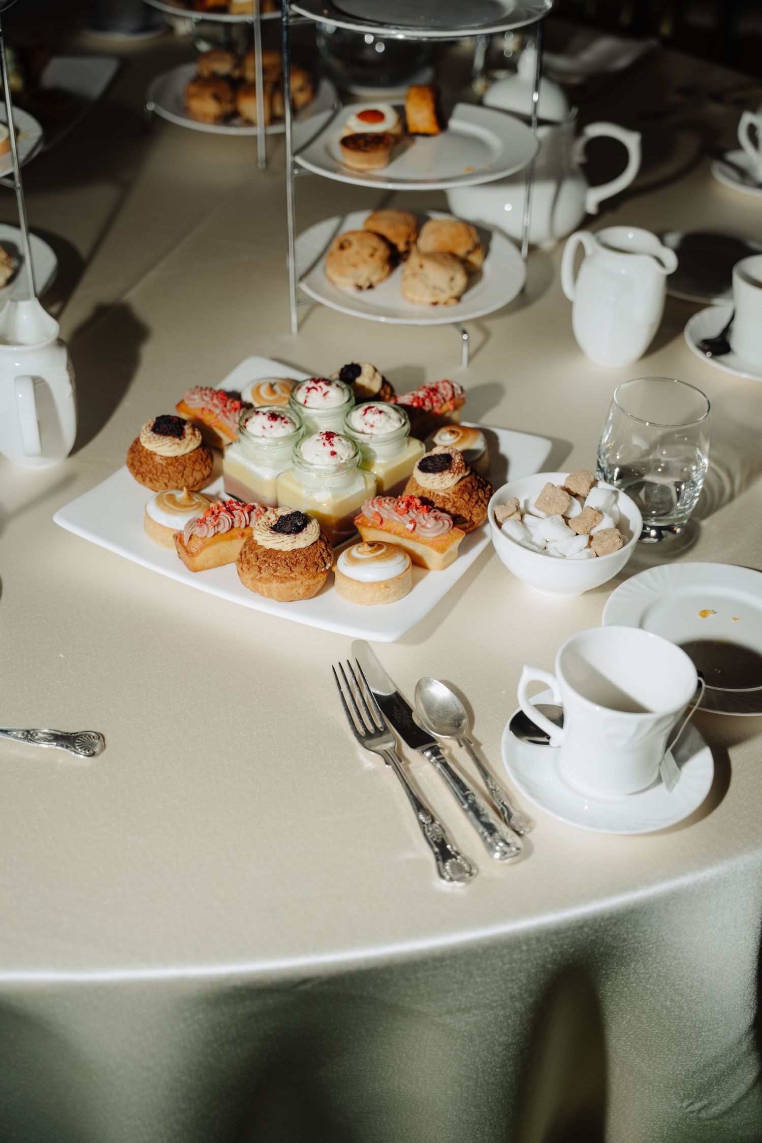 Elegant afternoon tea service with pastries and desserts arranged on white tablecloth with fine china and silverware.