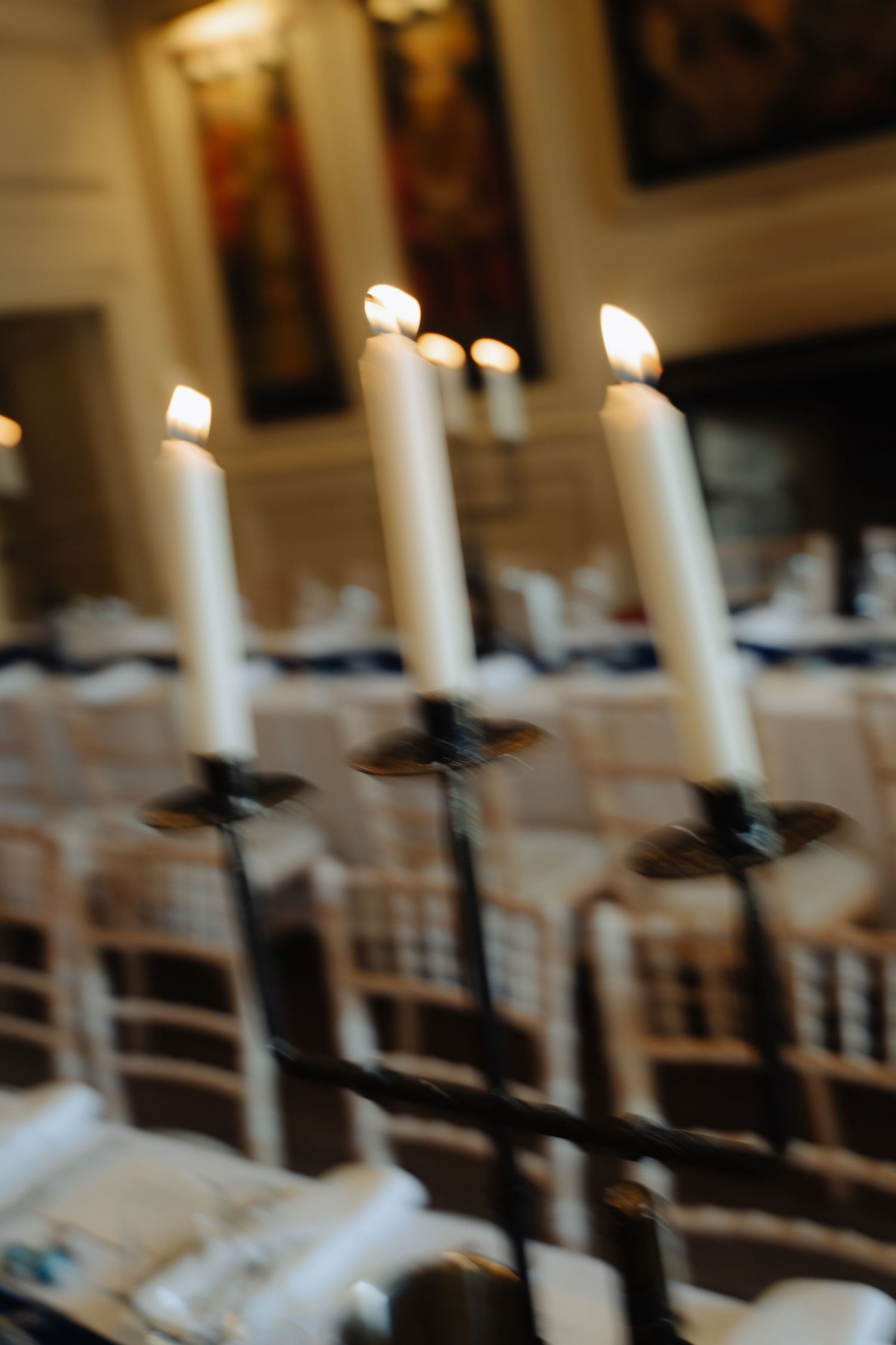 White candles line up along elegant chairs at a formal event venue with soft bokeh lighting in the background.