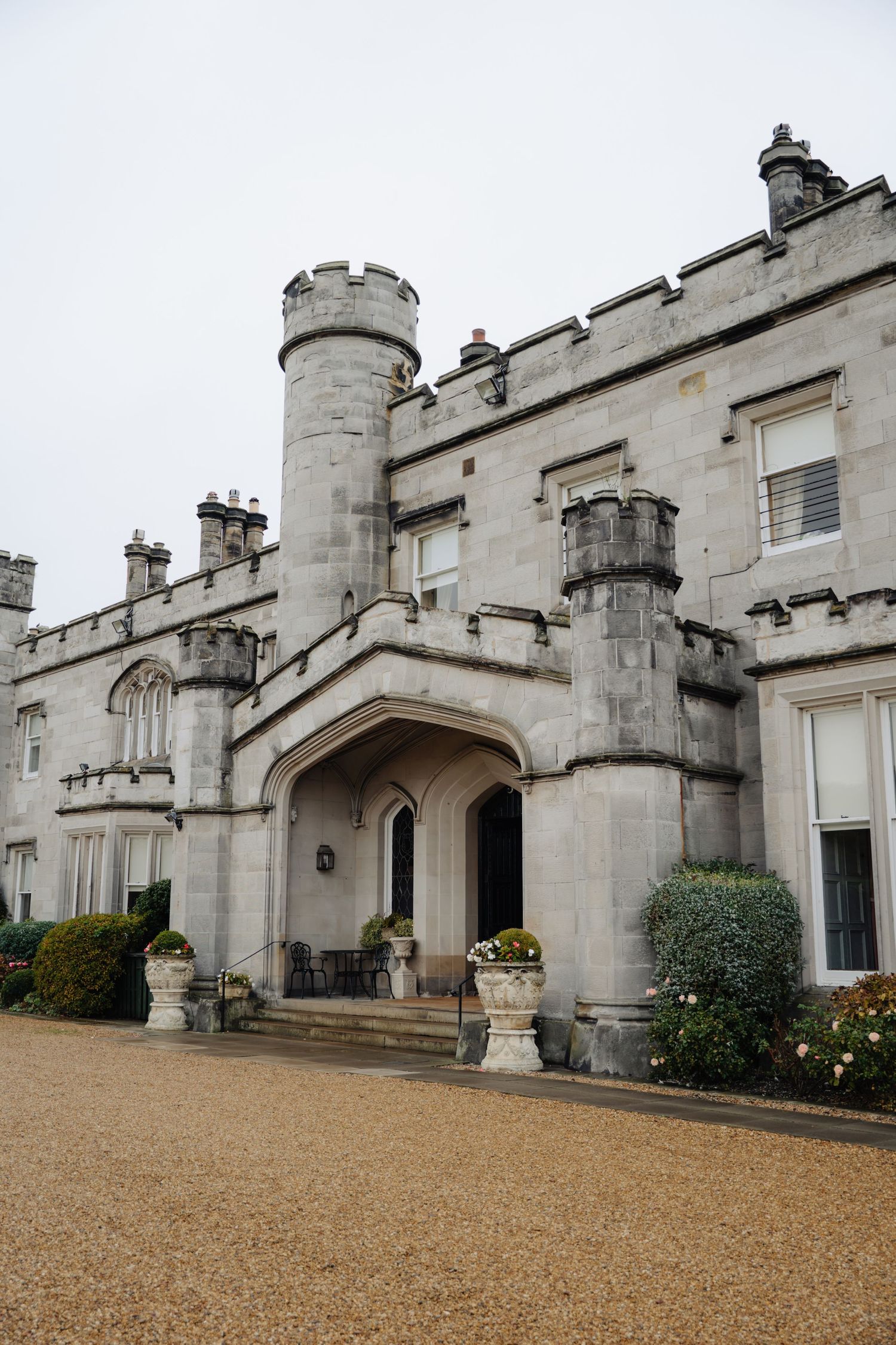 Dundas castle entrance with stone turrets, arched doorway and gravel driveway on an overcast day.