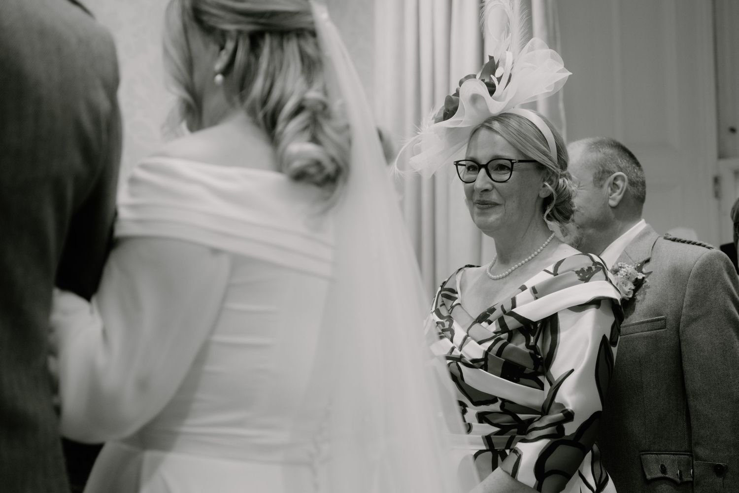 A black and white candid photograph of guests interacting at a formal indoor event.