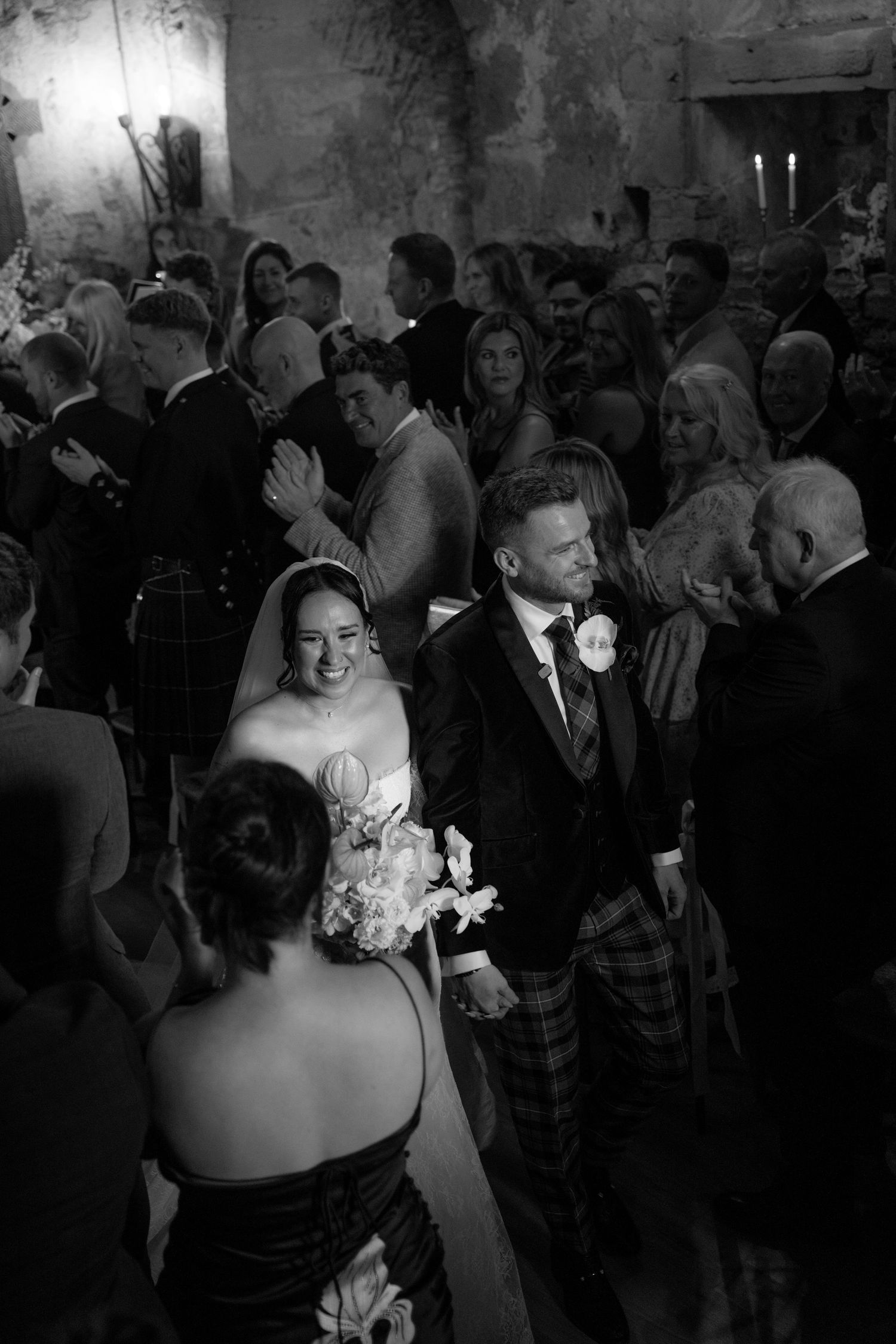 Black and white photo of smiling bride and groom walking down the aisle at a wedding ceremony.