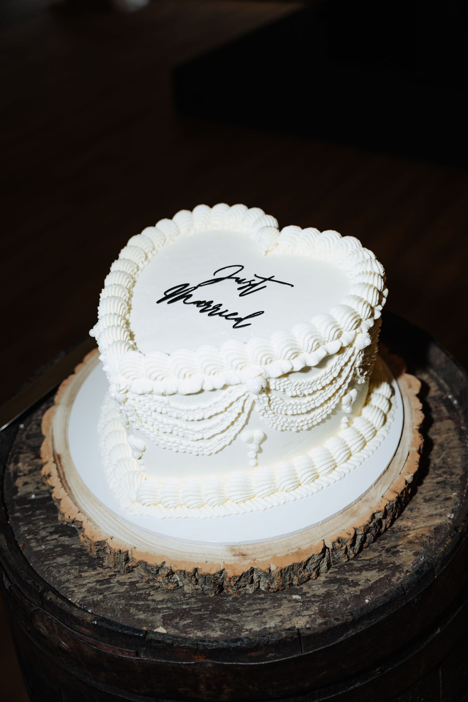 A white frosted cake with decorative piping sits on a dark rustic wooden base. Glasgow Engine Works