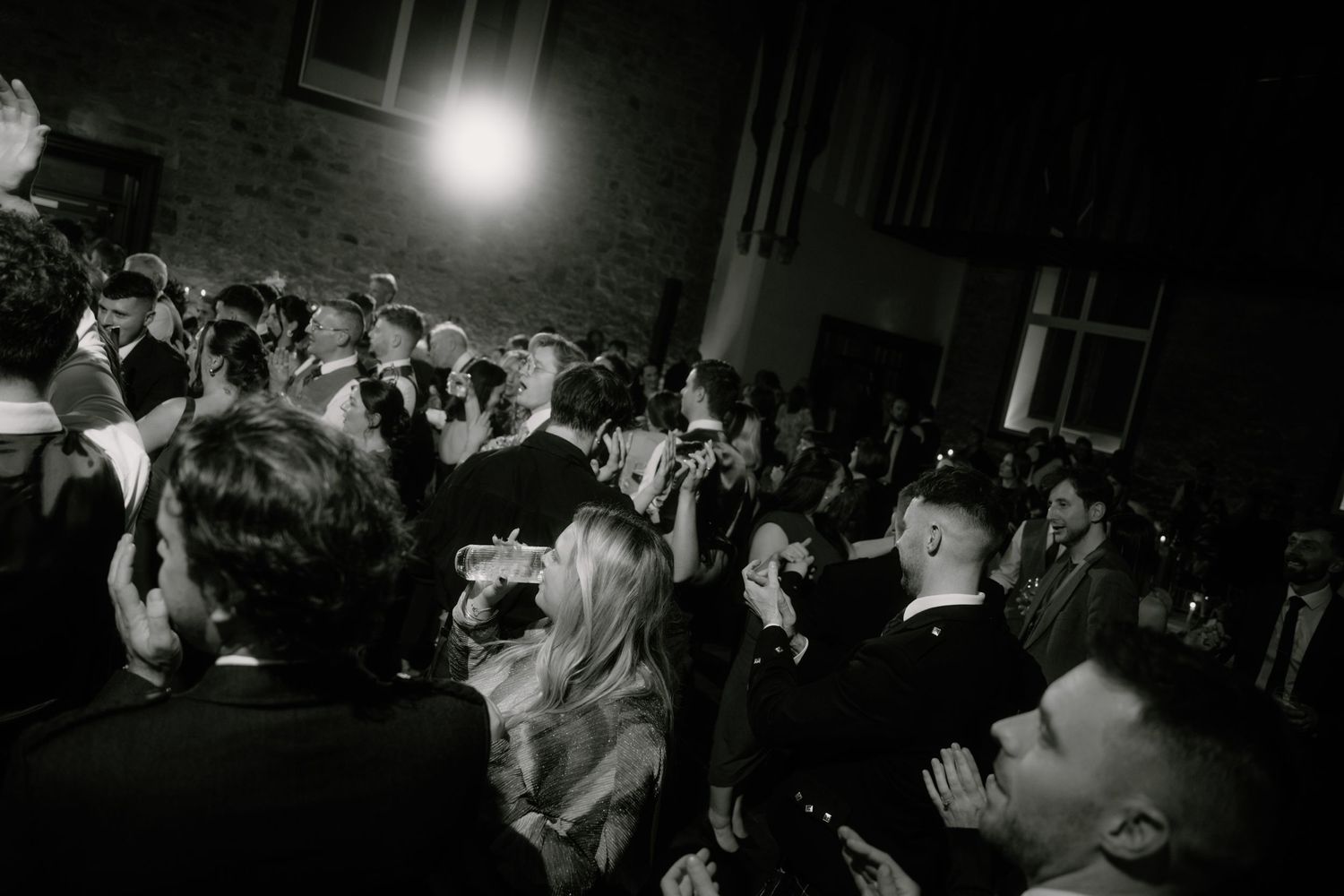 Black and white shot of a crowded dance floor at a celebration event with dramatic lighting.