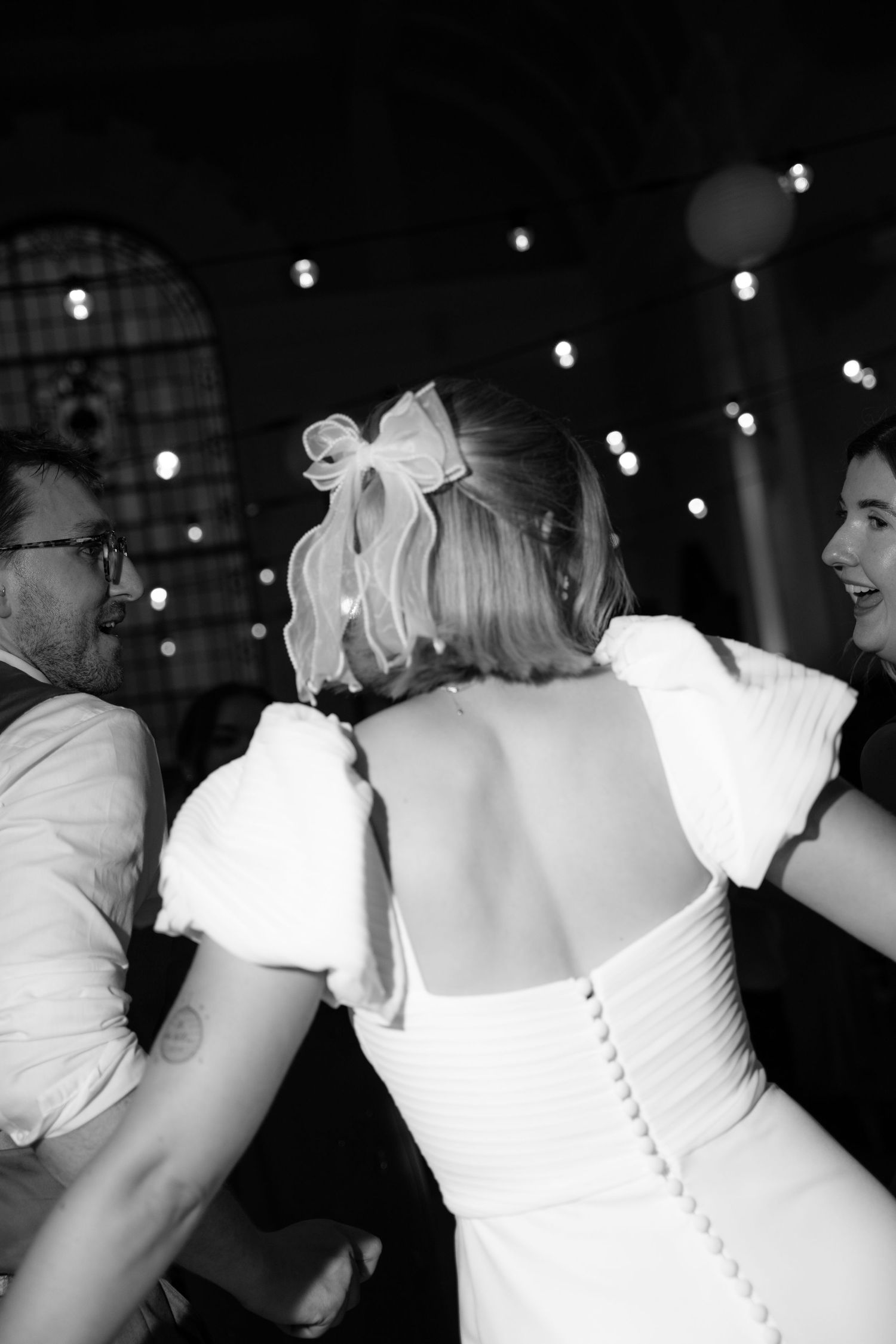 Black and white photo of a bride in a backless white gown with puff sleeves and bow hair clip dancing at her wedding reception.