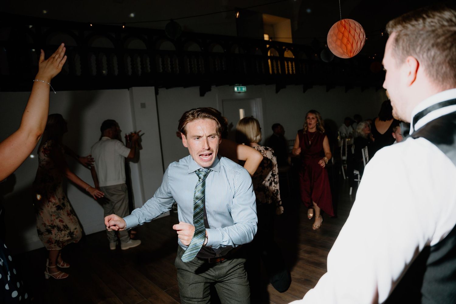 People dancing and celebrating at a dimly lit reception venue with festive party atmosphere.