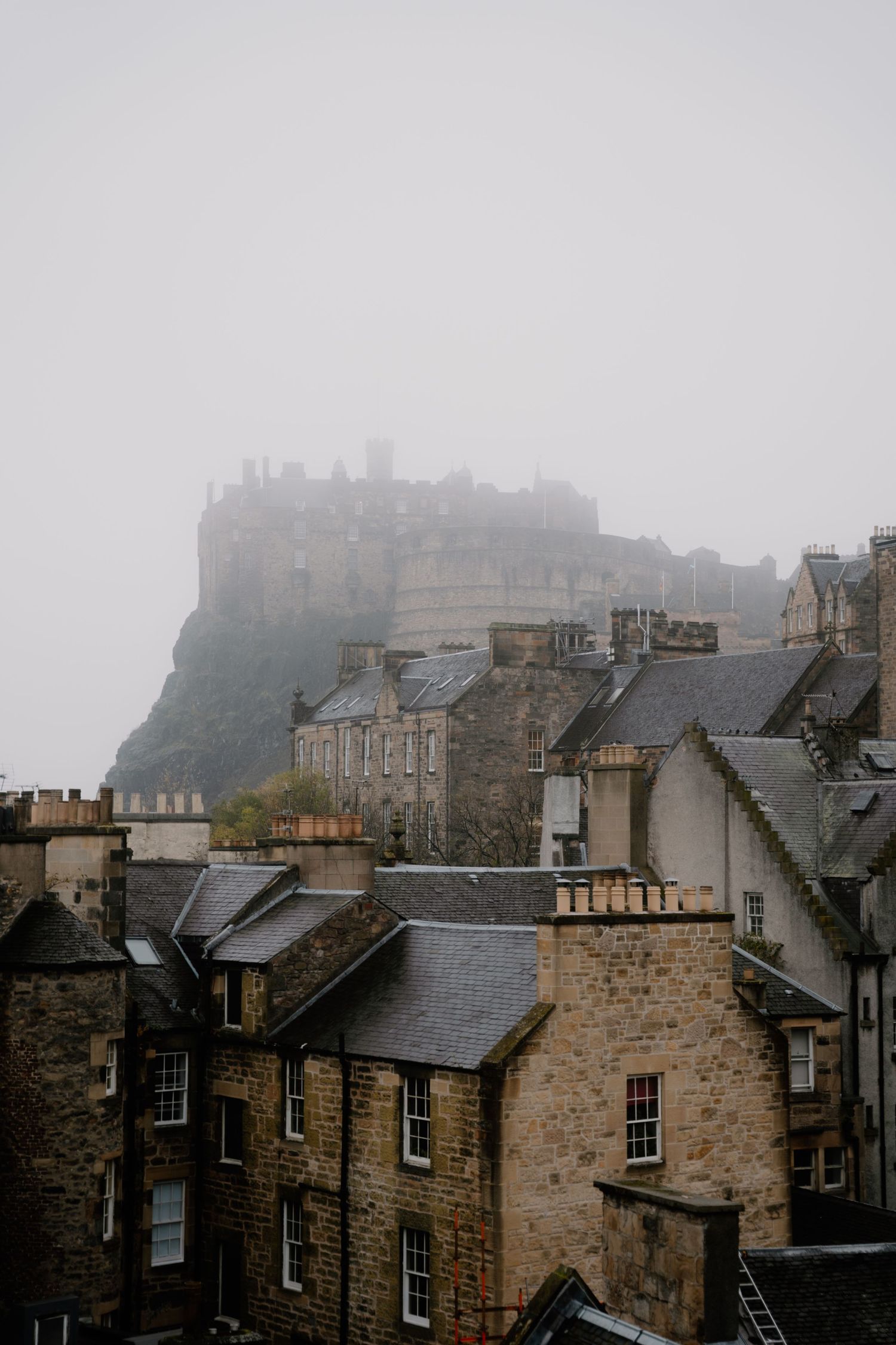 Foggy view of Edinburgh Castle perched atop a hill with historic buildings below.