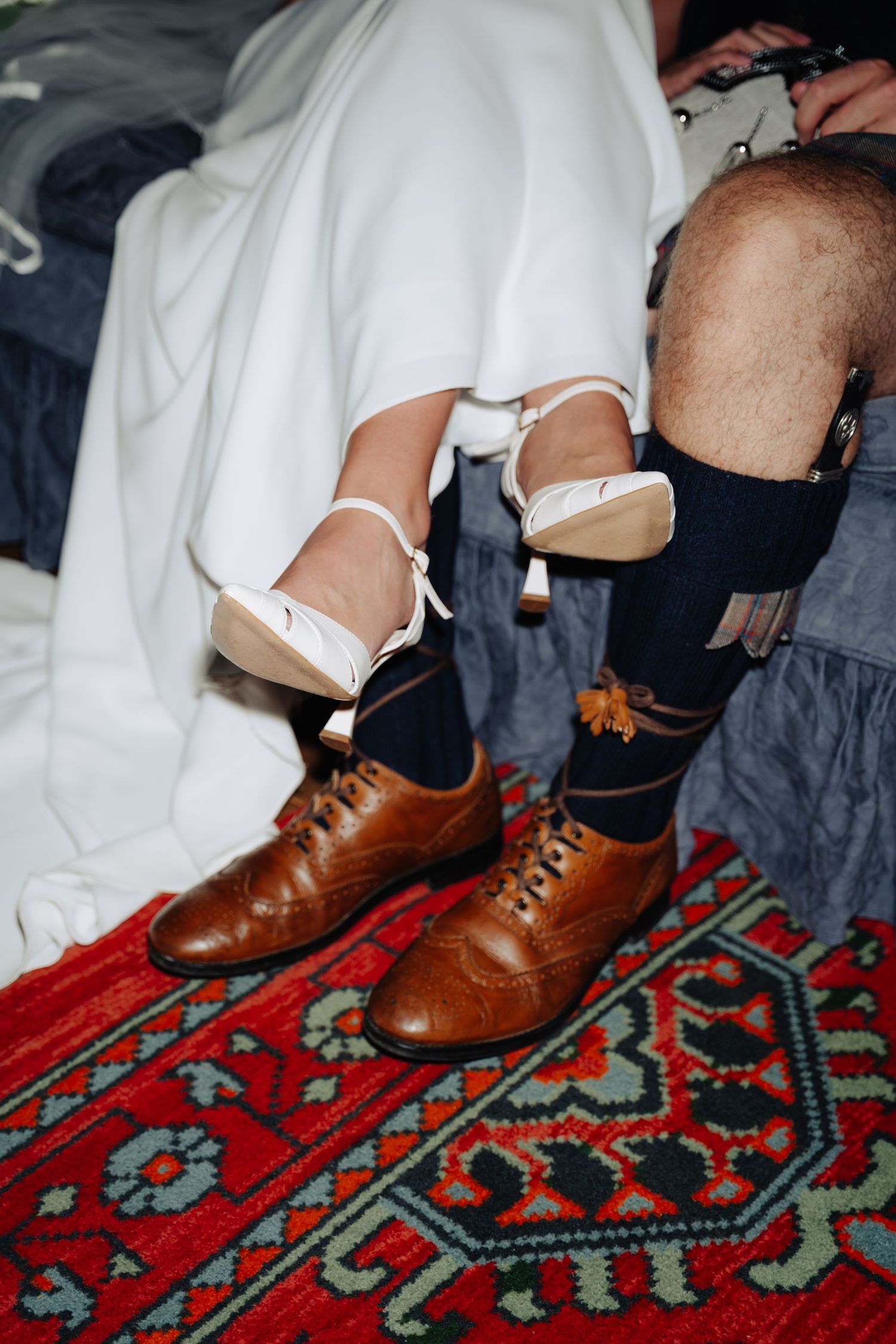 Brown leather oxford shoes paired with ripped jeans and white socks on a vibrant red patterned oriental rug.