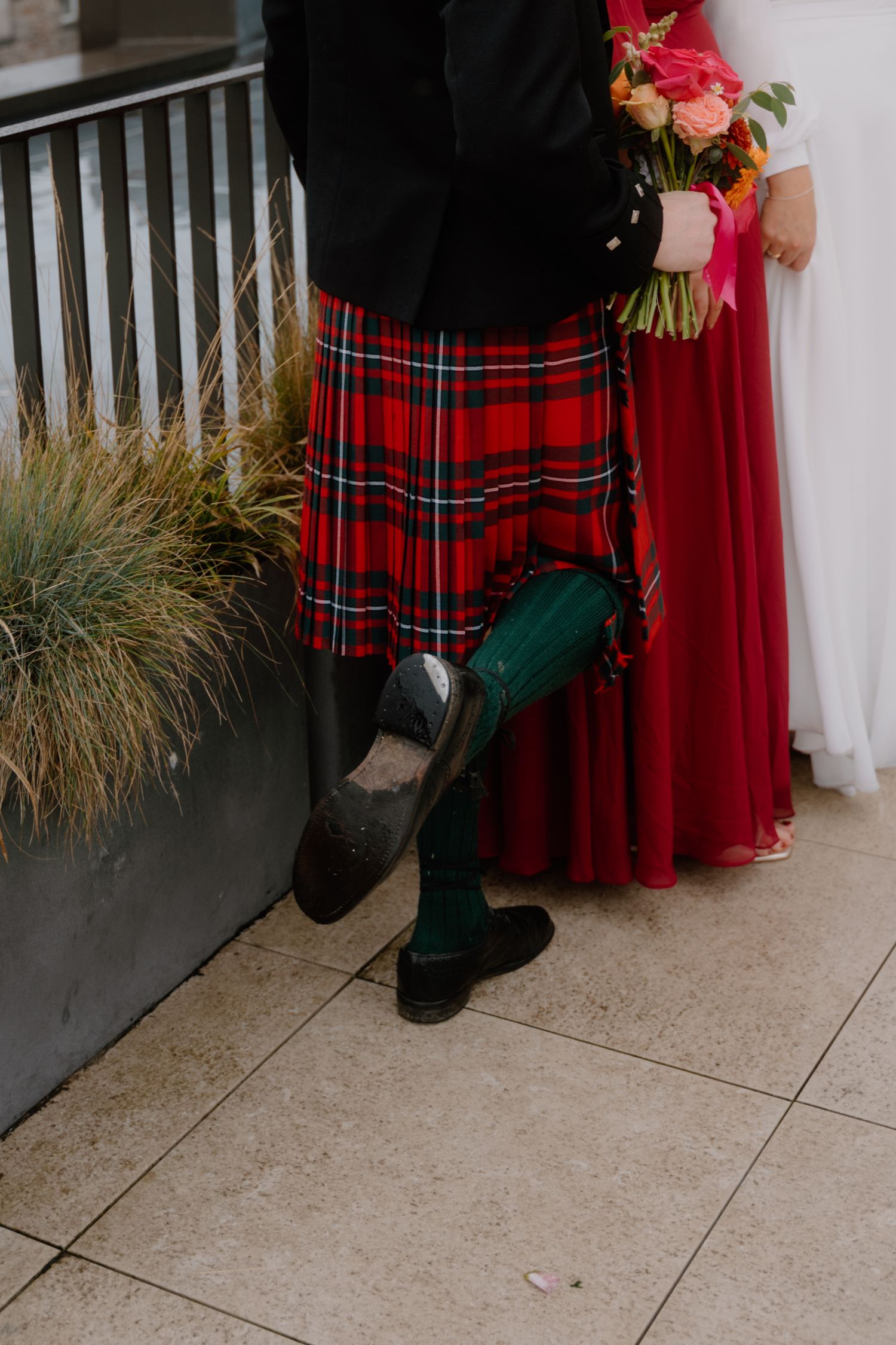 Detail shot of traditional red tartan kilt with green socks against formal attire.