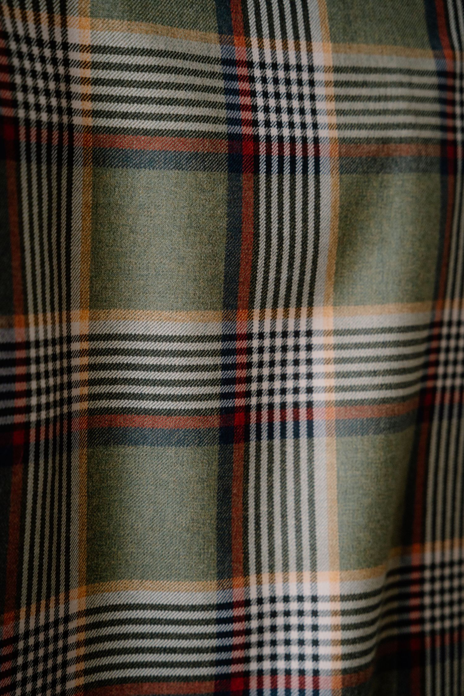 Close-up detail of green and orange plaid fabric pattern with intersecting lines.