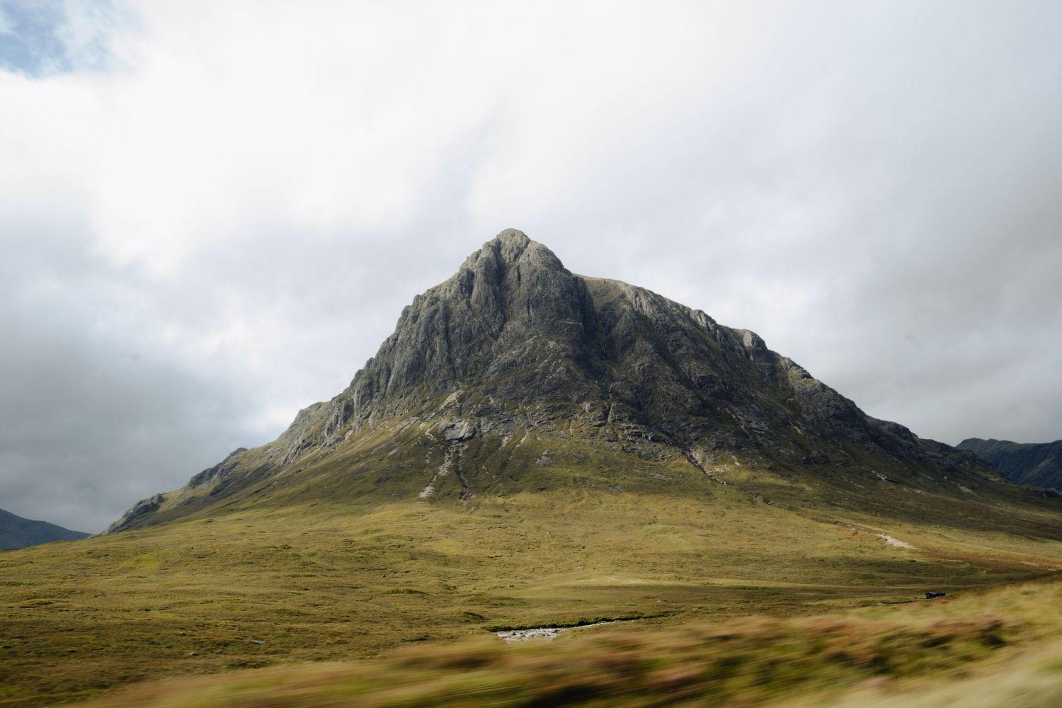 A panoramic view of rugged mountain peaks with rocky outcrops and grassy slopes under a cloudy sky.