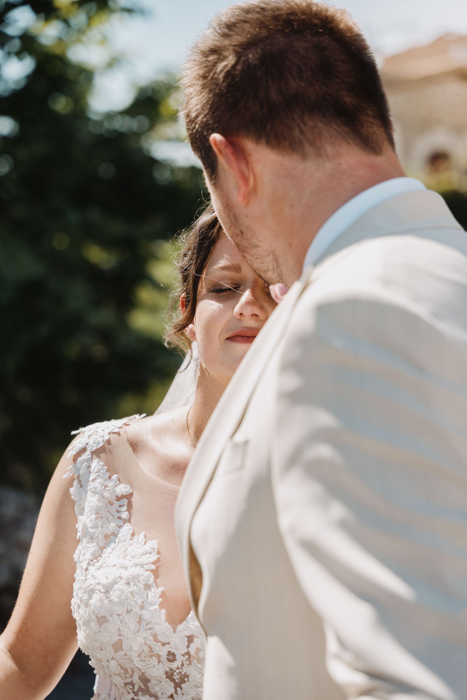 Groom kisses bride on forehead as she closes her eyes in a tender outdoor wedding moment.