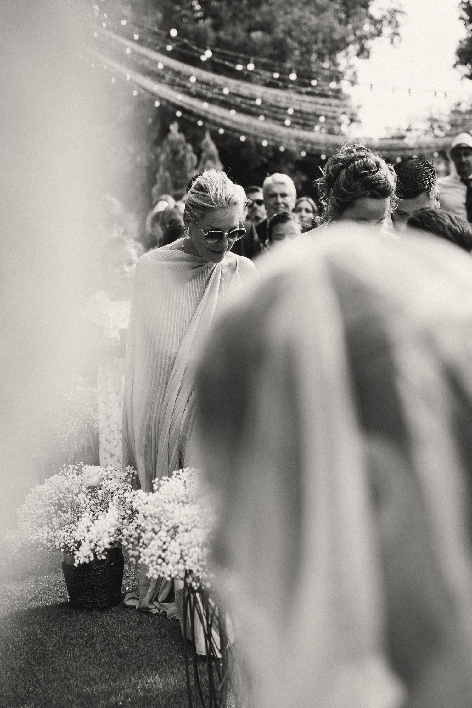 Black and white photo of wedding guests gathered outdoors under string lights during ceremony.