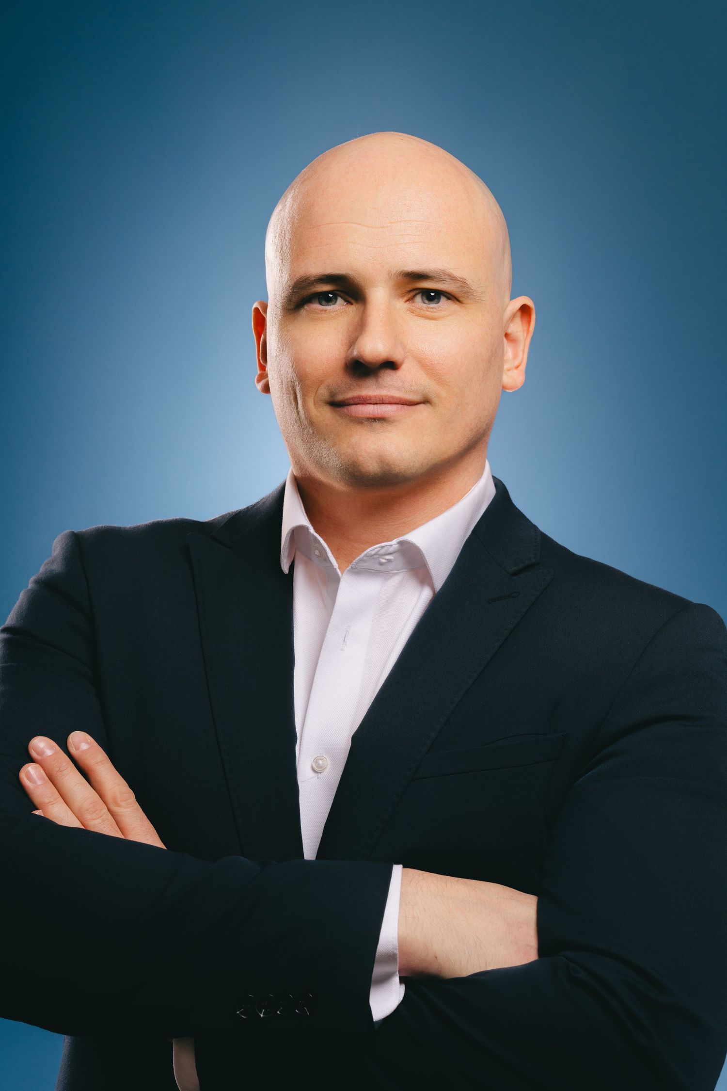 Confident bald man in black suit with arms crossed against blue gradient background.