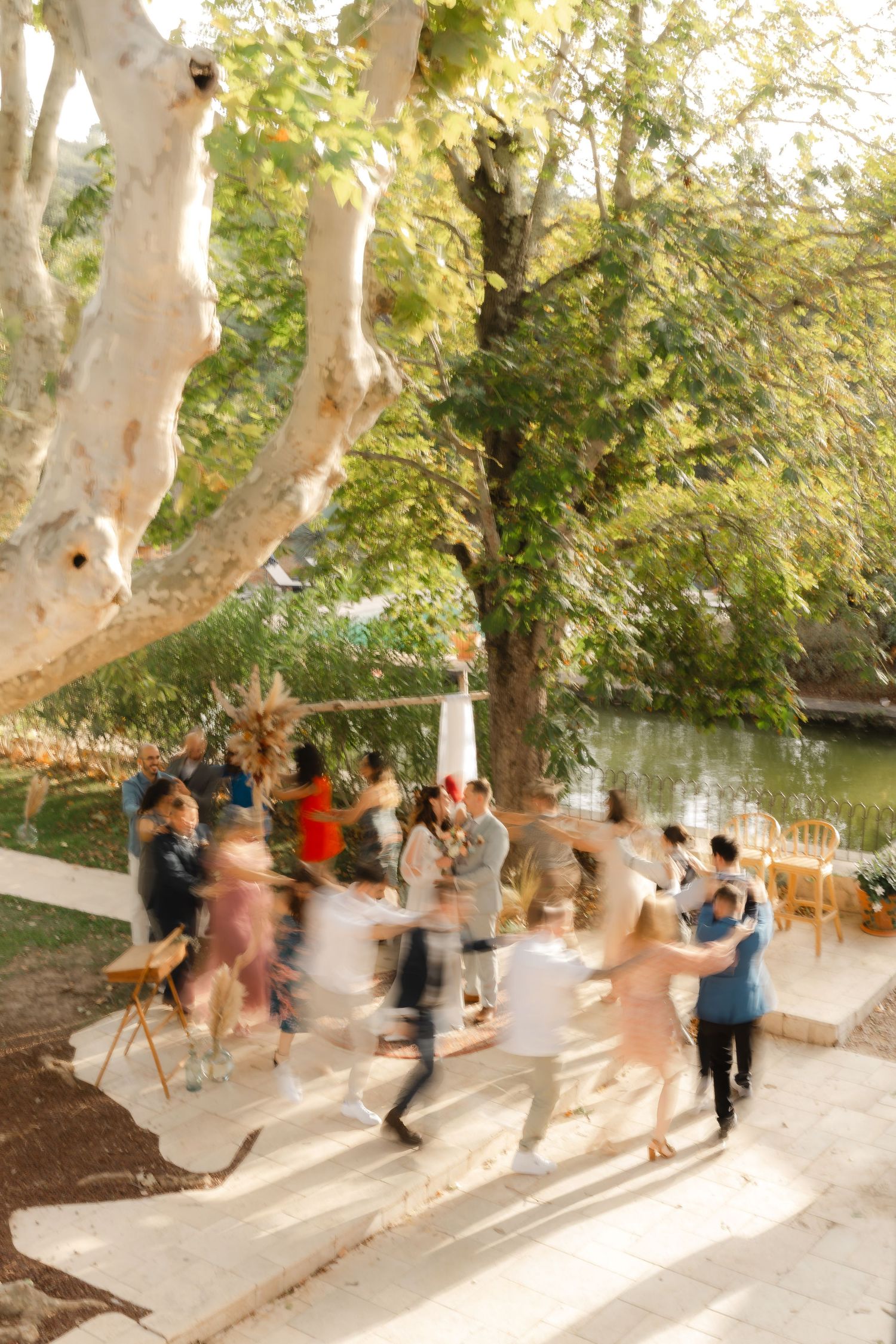 Guests dancing outdoors at a garden wedding reception near a river, surrounded by lush green trees.