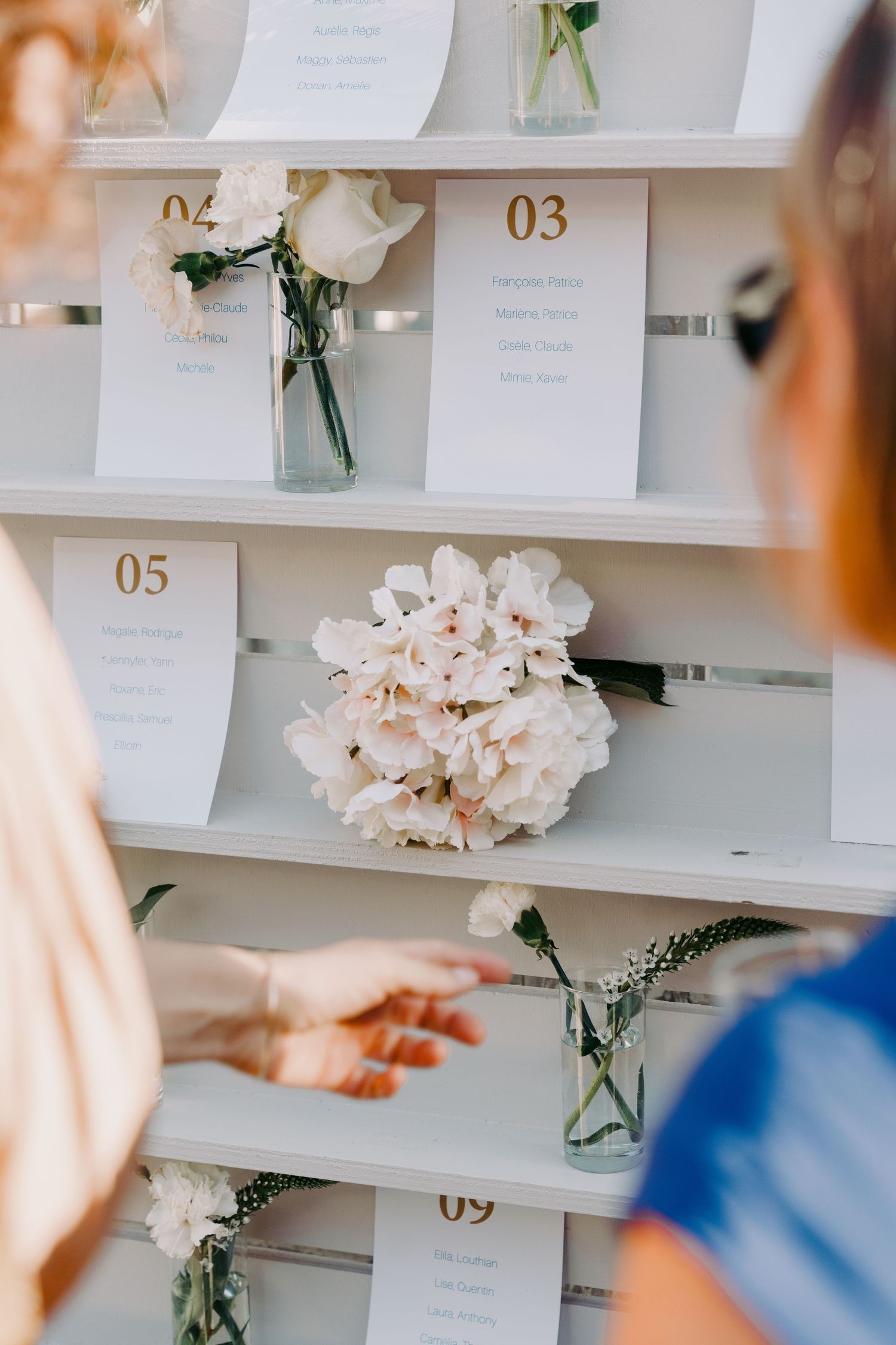 Wedding seating chart display on white shelves decorated with white hydrangeas and roses. Wedding detail