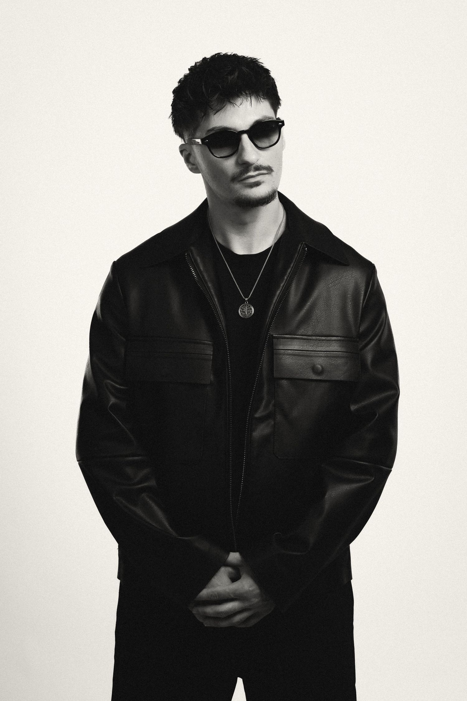 Black and white portrait of a young man in a leather jacket and sunglasses with a chain necklace.