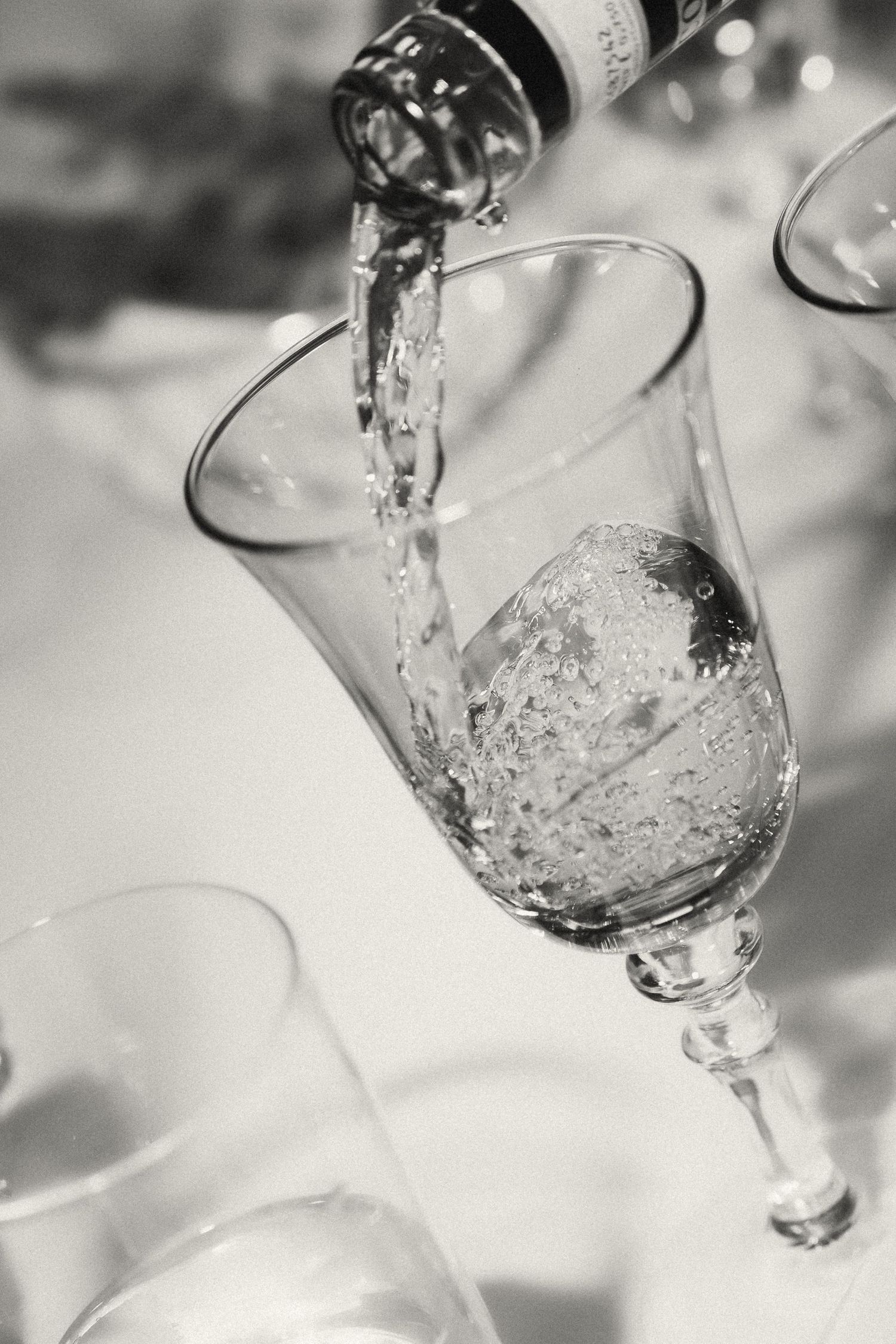 Black and white close-up of sparkling wine being poured into an elegant crystal glass.