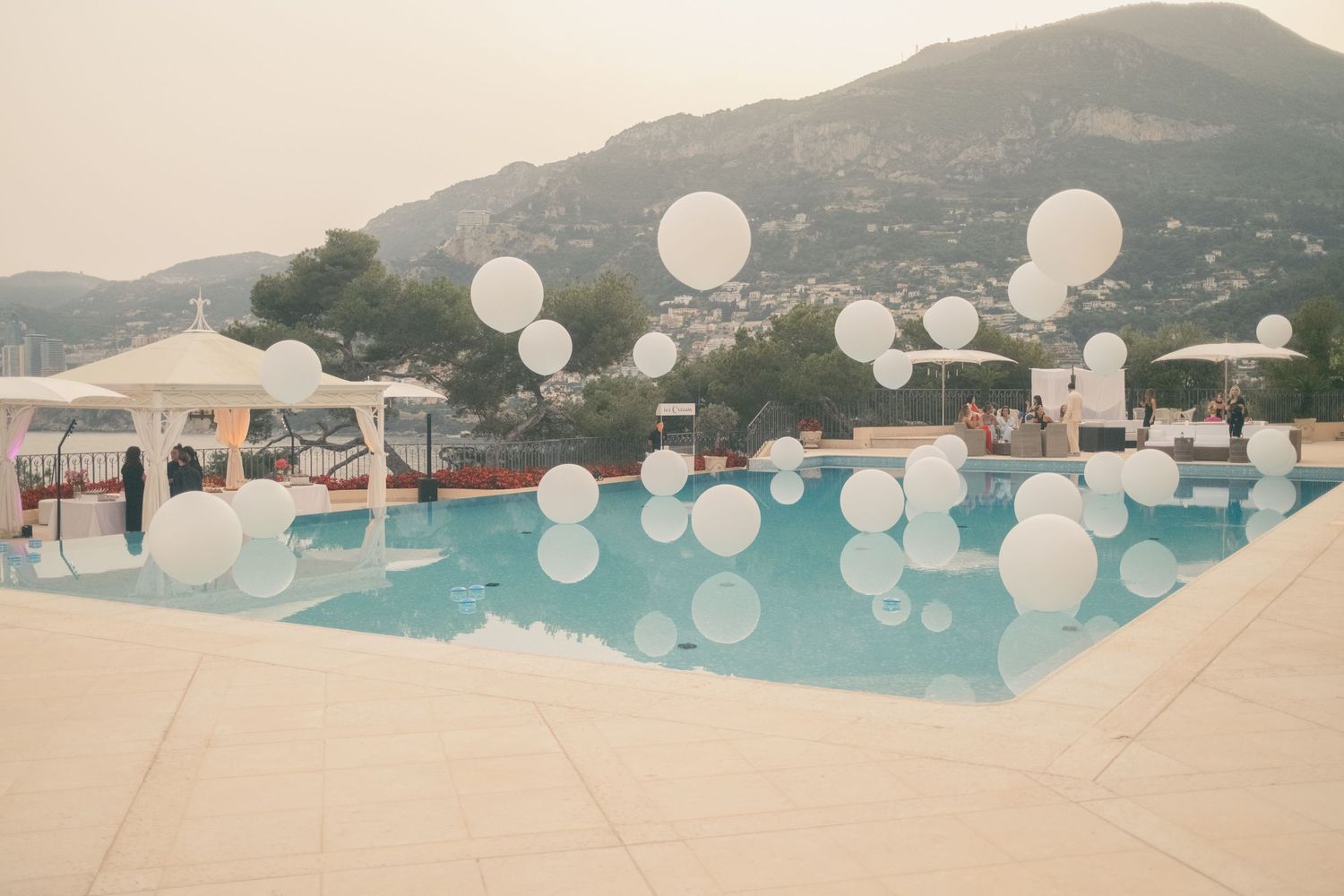 White balloons float over a serene outdoor pool with mountain views at an elegant event venue.